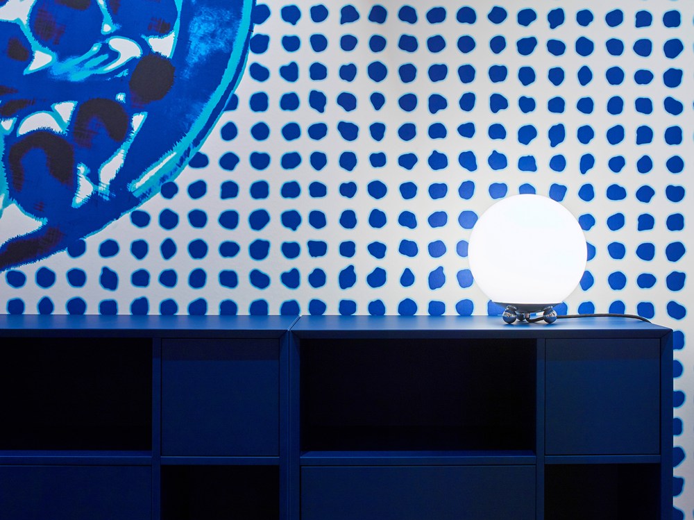 Art Déco Tischleuchte AD32 von Tecnolumen mit Opalglas-Schirm auf blauem Sideboard vor gemusterter Tapete.
