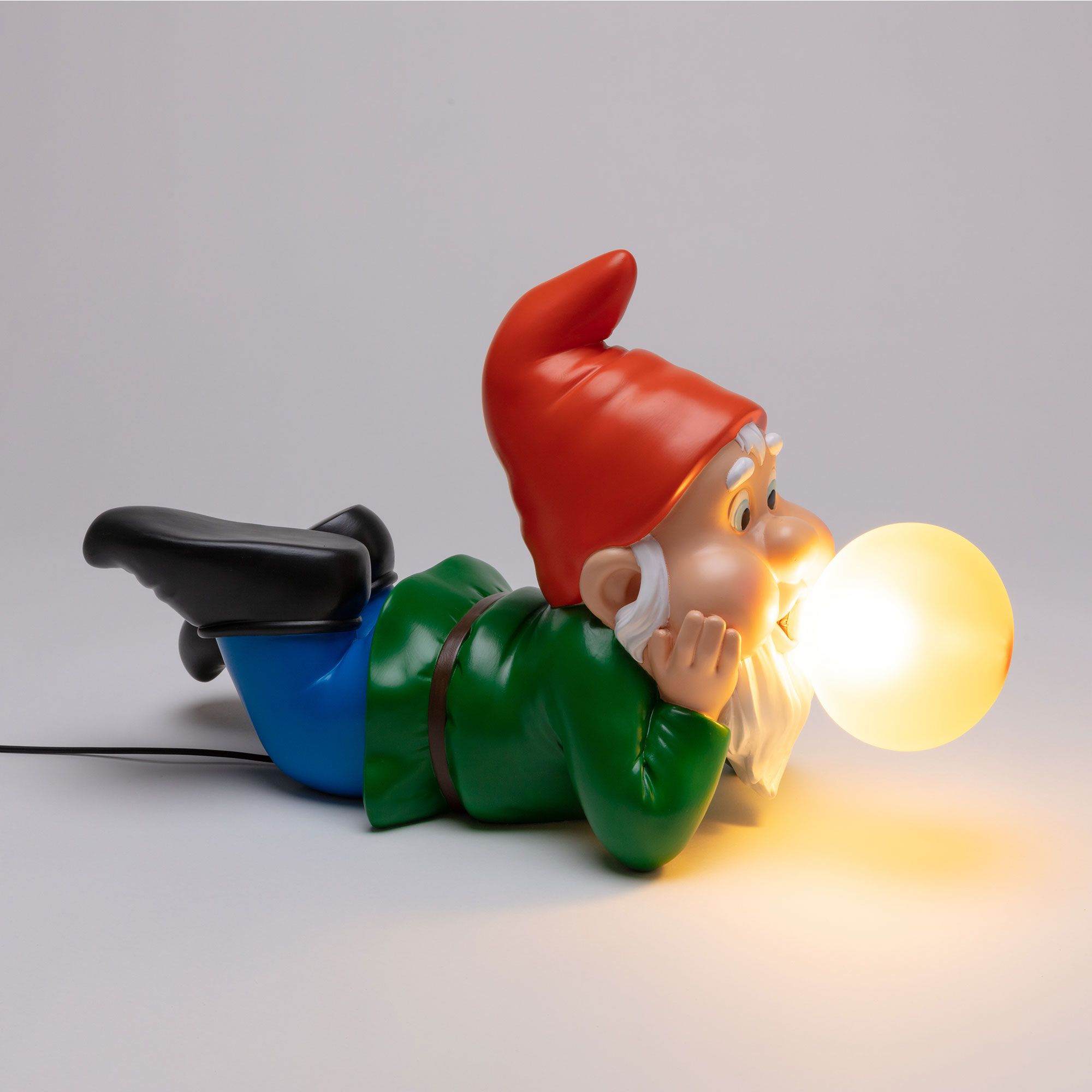 Gummy Dreaming Leuchte von Seletti: Liegender Gartenzwerg mit roter Mütze und leuchtender Kugel als Lampe.