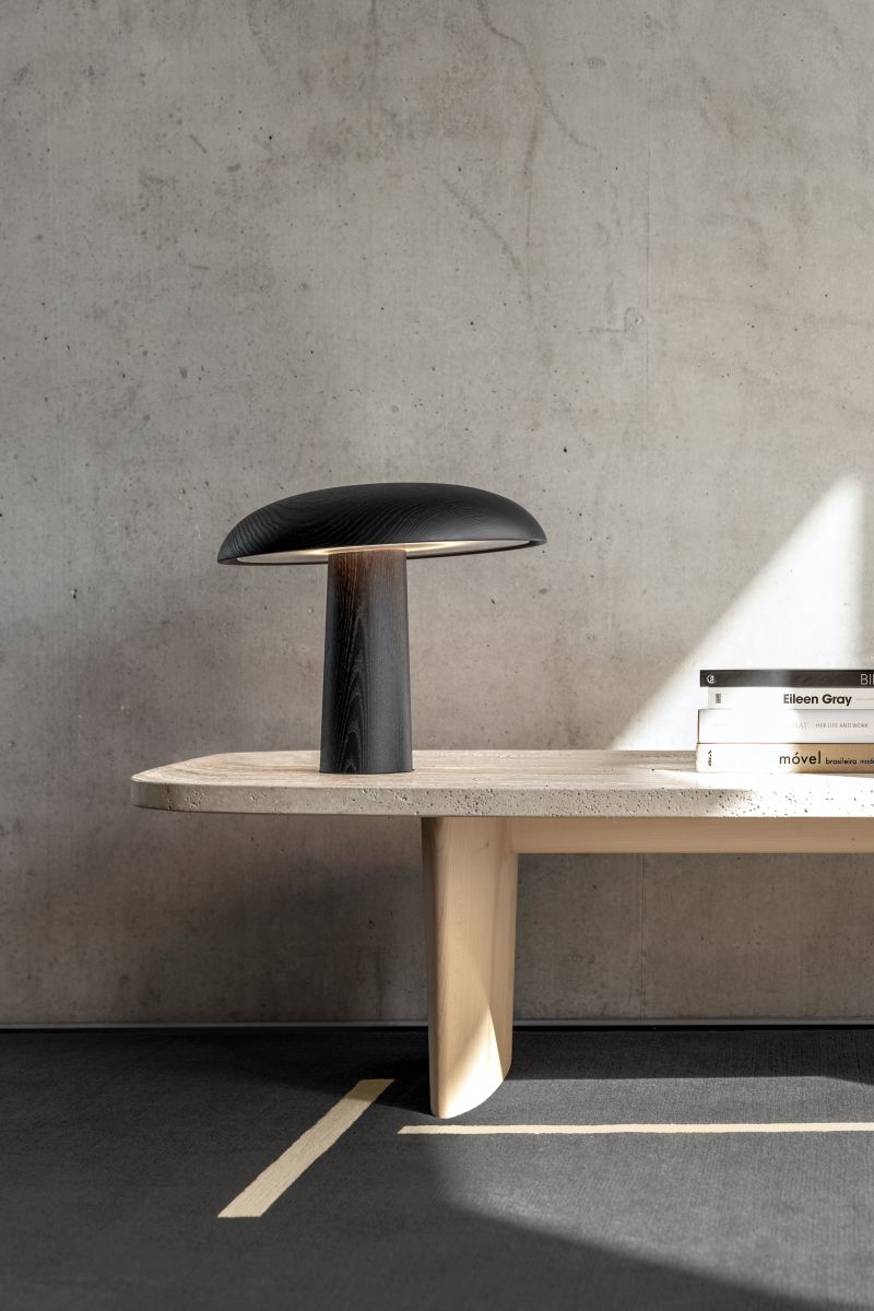 Nahaufnahme der ClassiCon Bell Tischleuchte aus Holz auf einem Betontisch mit Büchern.