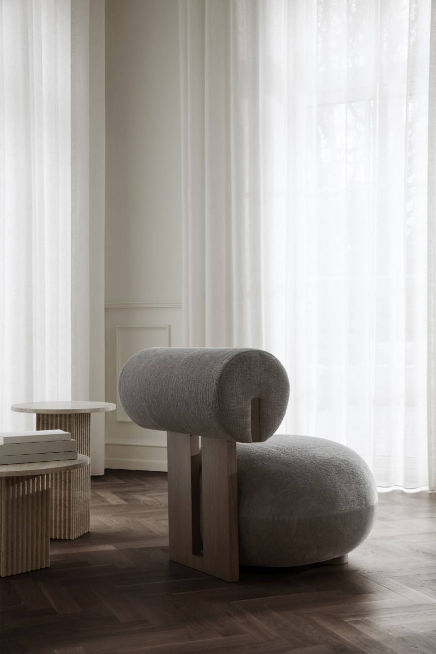 Grauer Hippo Lounge Chair Sessel von NORR11 mit Holzgestell vor hellem Vorhang und dunklem Holzboden.