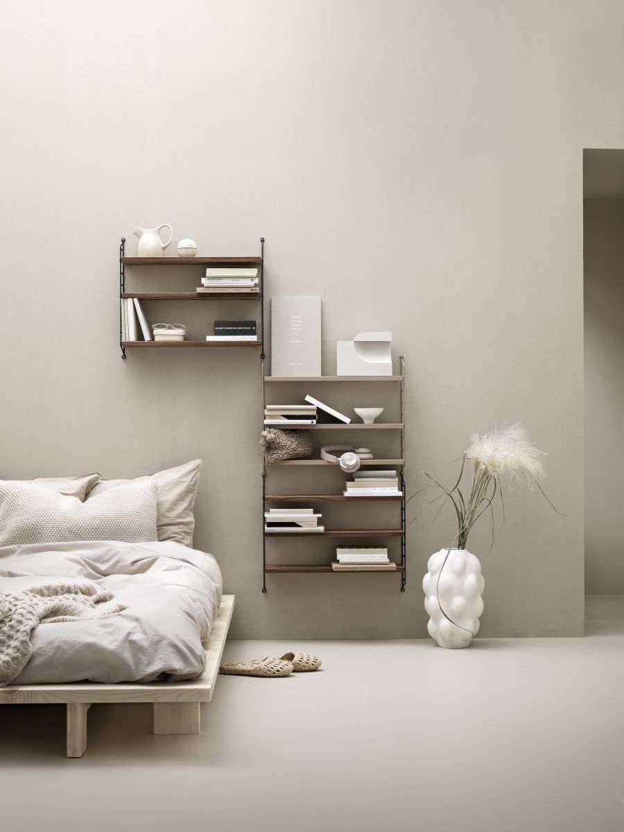Schlafzimmer mit minimalistischem Bett, String Regalsystemen in Holz und Deko-Elementen für moderne Wandgestaltung.