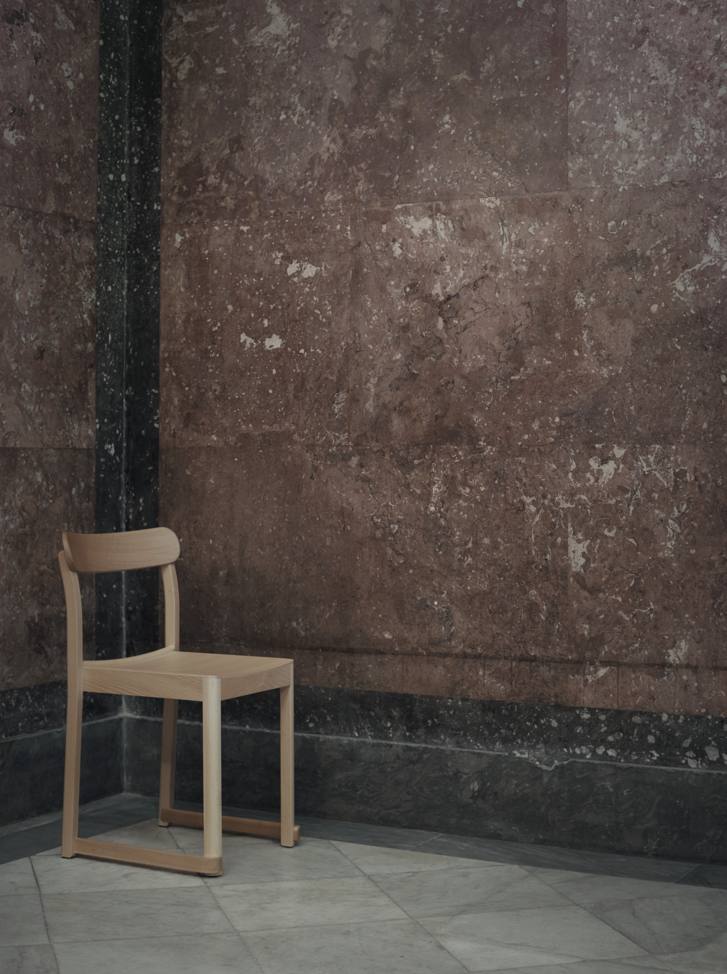 Atelier Chair Stuhl von Artek, helles Holz, minimalistisches Design vor einer roten Marmorwand.