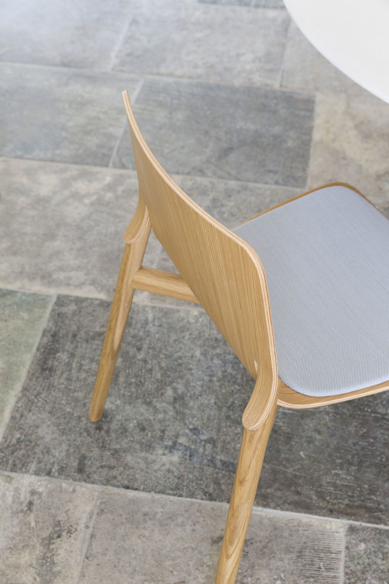 Detailaufnahme des Kayak Holzstuhls mit grauem Sitzpolster, ein moderner Holzstuhl für Esszimmer und Wohnbereich.