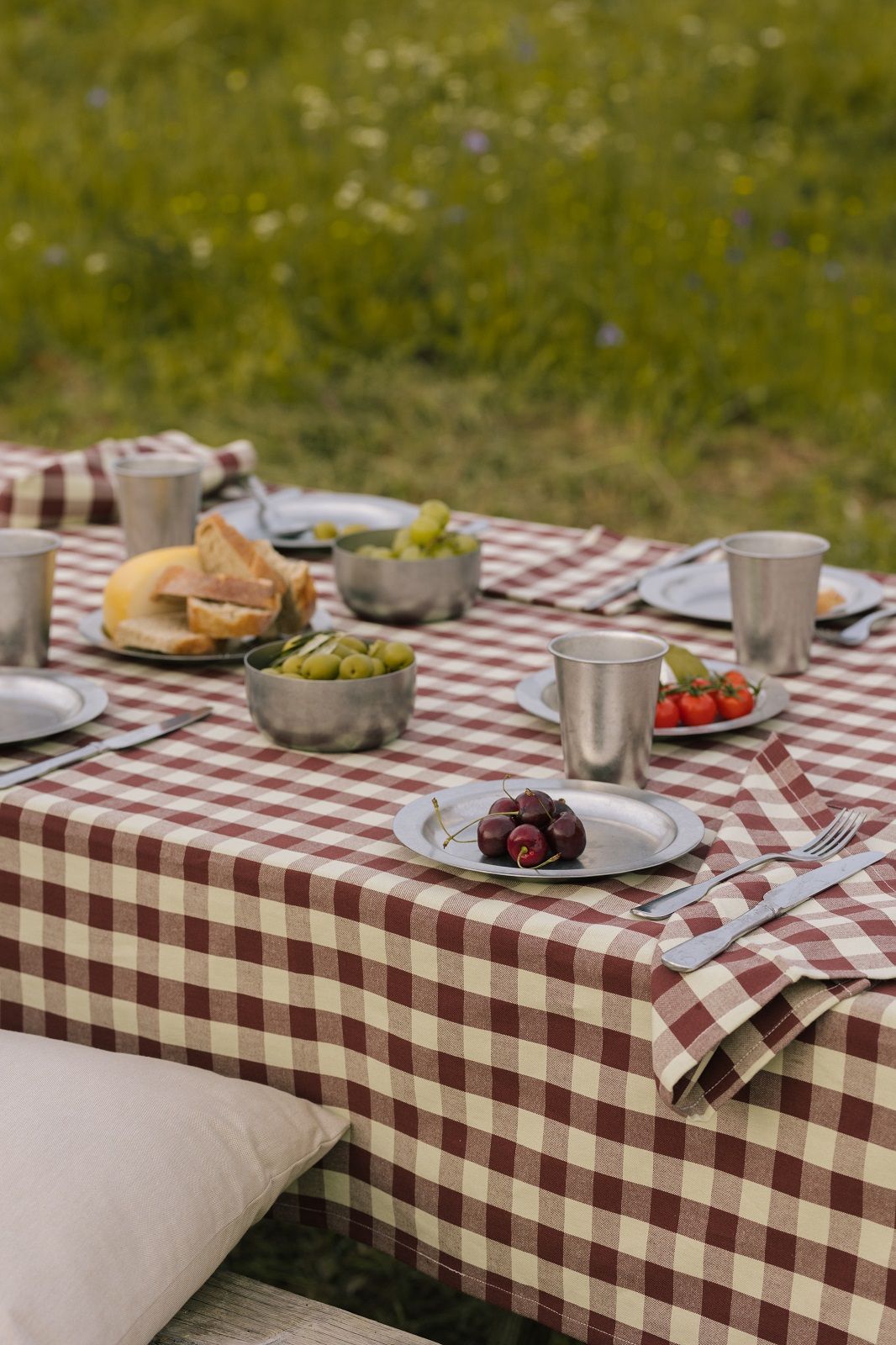 Nahaufnahme eines Picknicktisches mit Ferm Living Tellern, Speisen und Getränken im Freien.