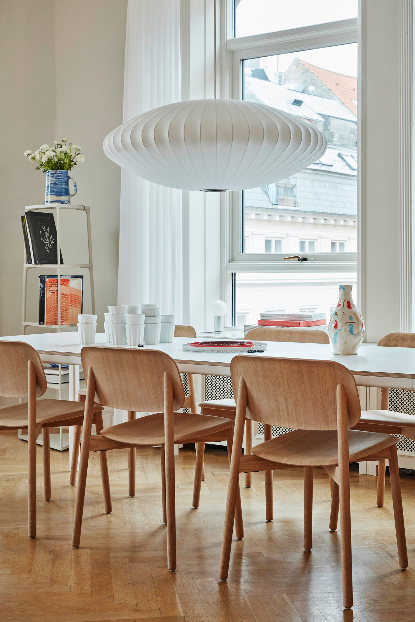 Esszimmer mit Hay Soft Edge 60 Stühlen aus hellem Holz um einen weißen Tisch mit Geschirr.