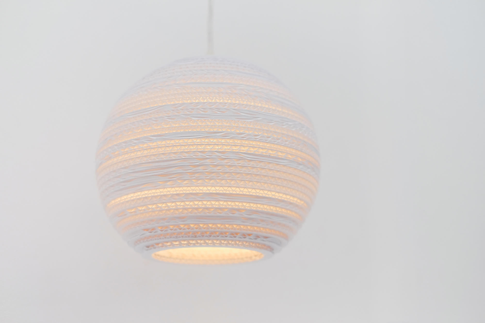 Weiße Scraplights Moon Hängeleuchte von Graypants aus recycelter Pappe, warmes Licht scheint durch die Lamellen.