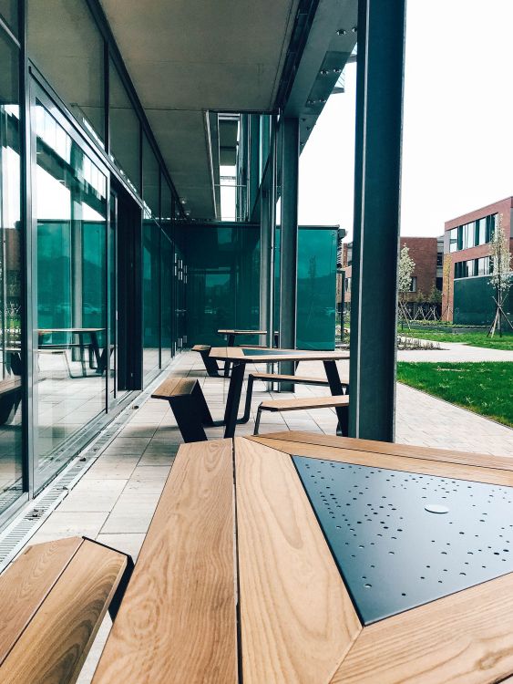 Außenbereich mit modernen Picknicktischen aus Holz und Metall vor einem Bürogebäude.