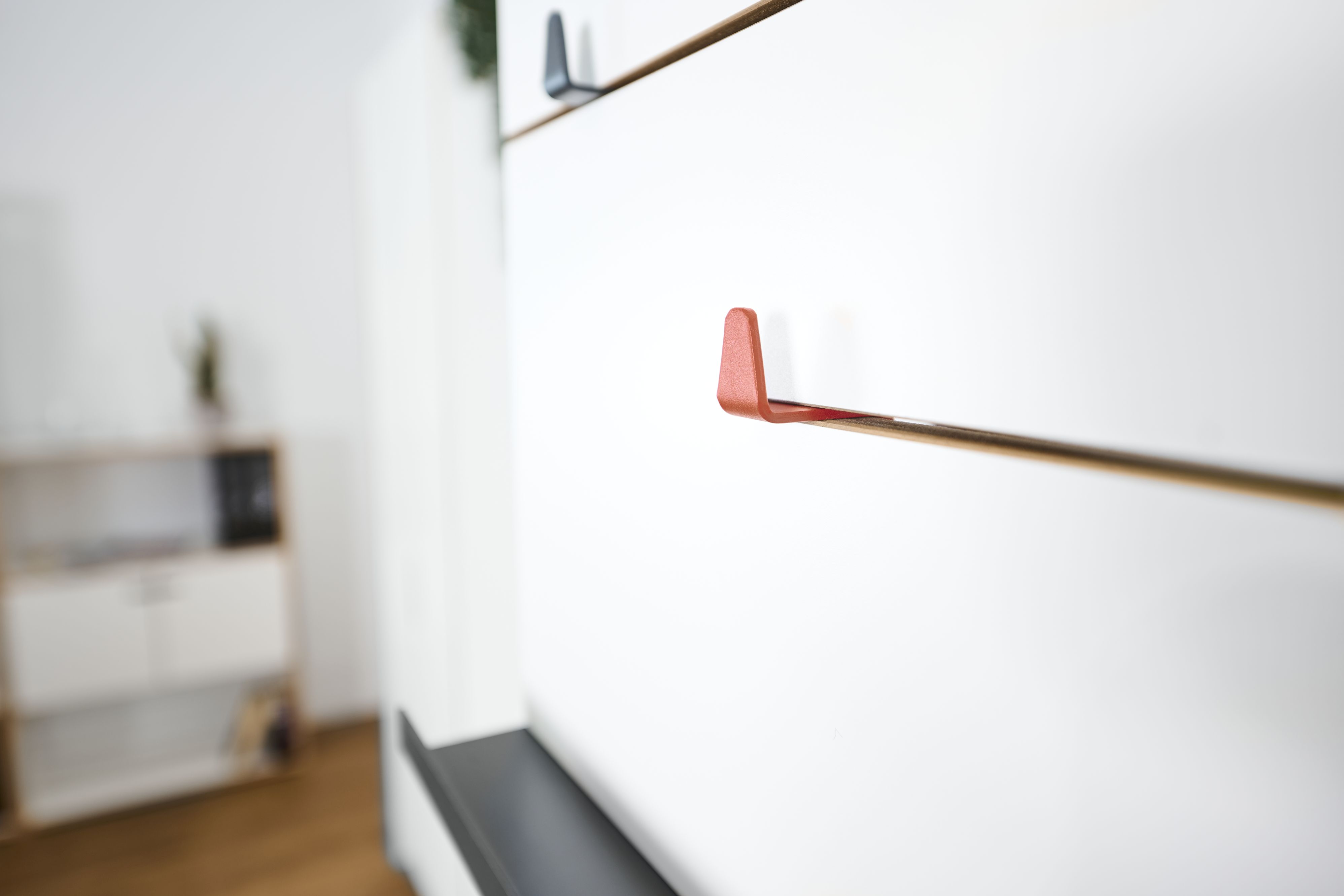 Nahaufnahme von drei farbigen Tojo Angeber Haken an einer weißen Wand.