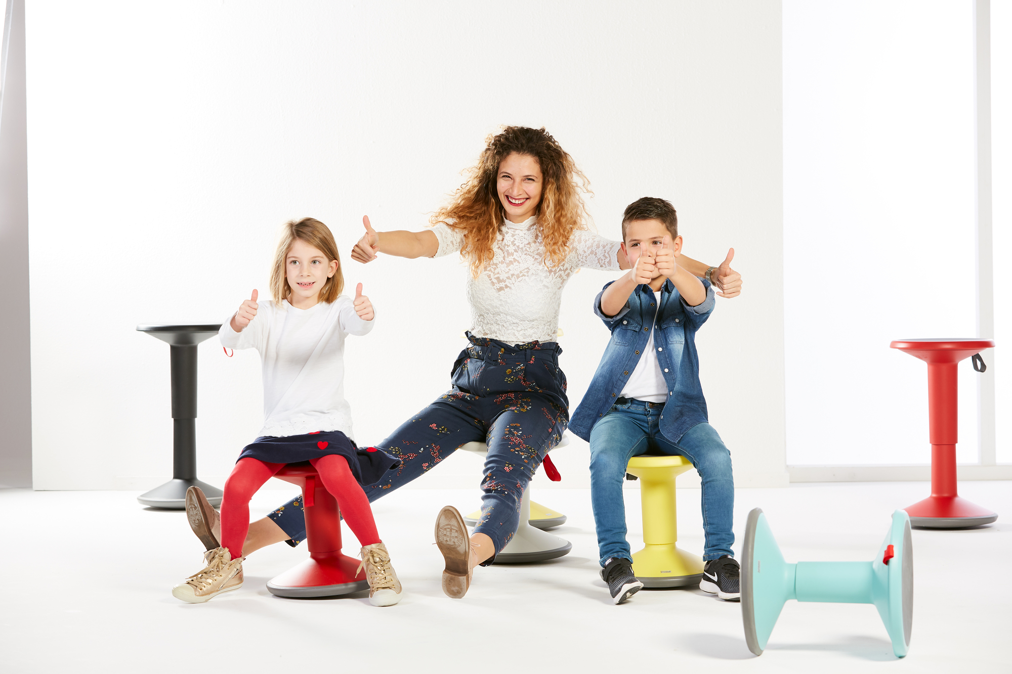 Kinder sitzen auf bunten UP Junior Edition Kinderhockern von Interstuhl und zeigen Daumen hoch.