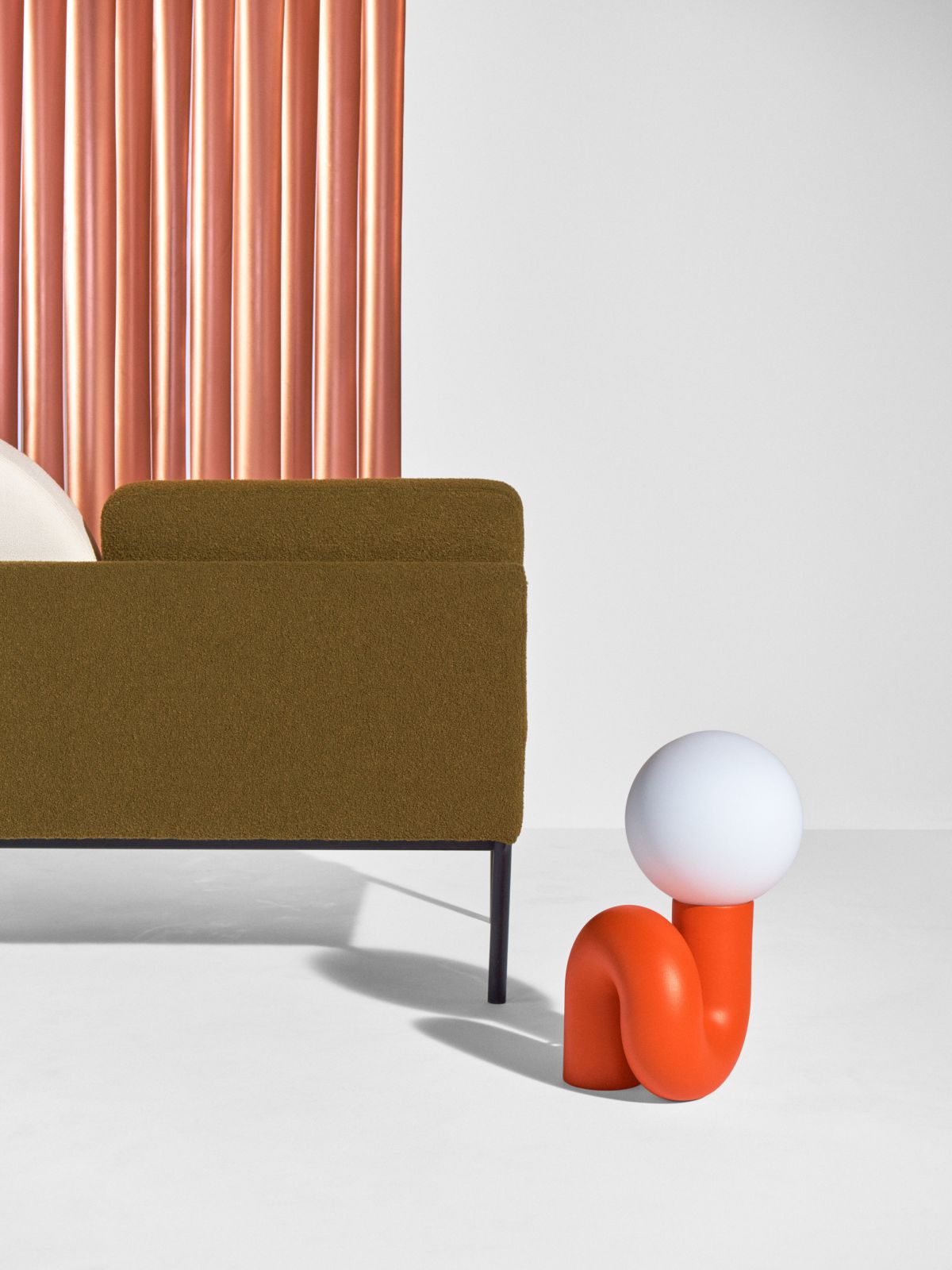 Nahaufnahme einer modernen, orangefarbenen Tischleuchte mit Kugel und olivgrünem Sofa. Designlampe für Wohnzimmer.
