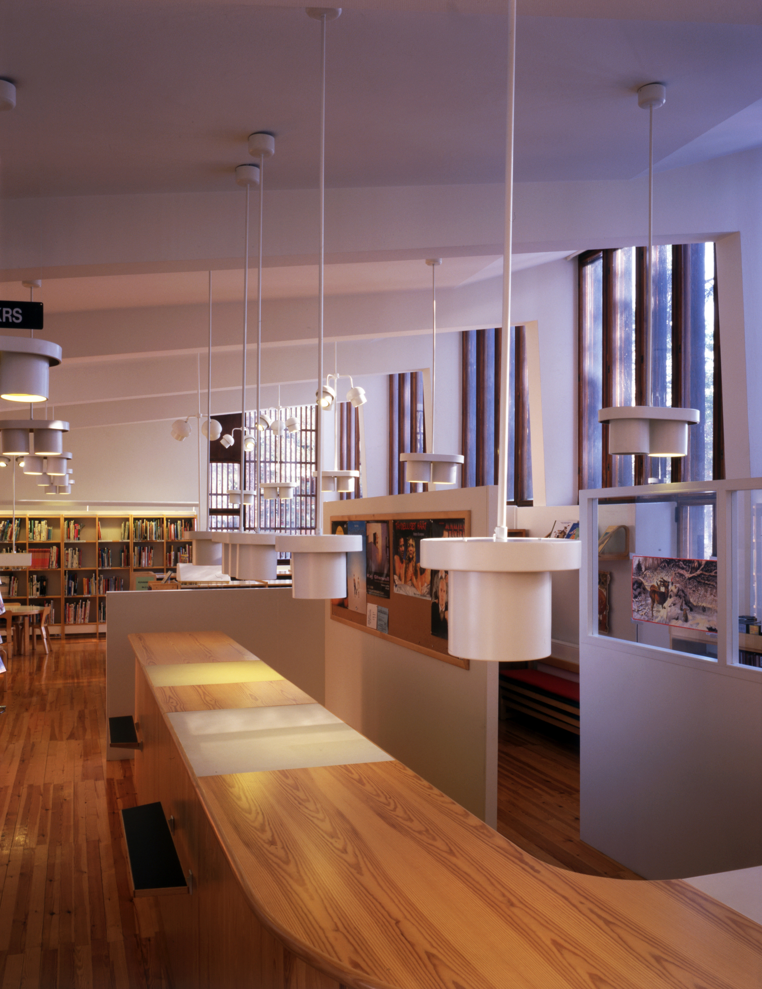Helle Bibliothek mit mehreren weißen A201 Pendant Light Pendelleuchten von Artek über einem langen Holztisch.