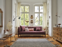 Wohnzimmer mit burgunderrotem Sofa und dekorativen Vitra Kissen in Rosa- und Lilatönen.