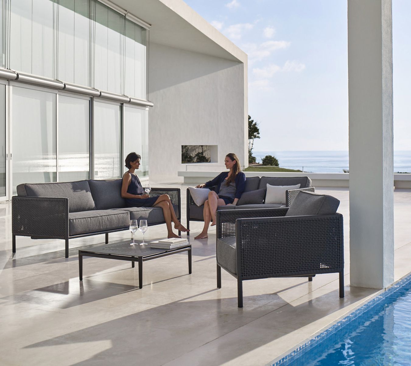 Encore Loungesessel von Cane-Line mit AirTouch Kissen auf Terrasse mit Meerblick. Outdoor Möbel.