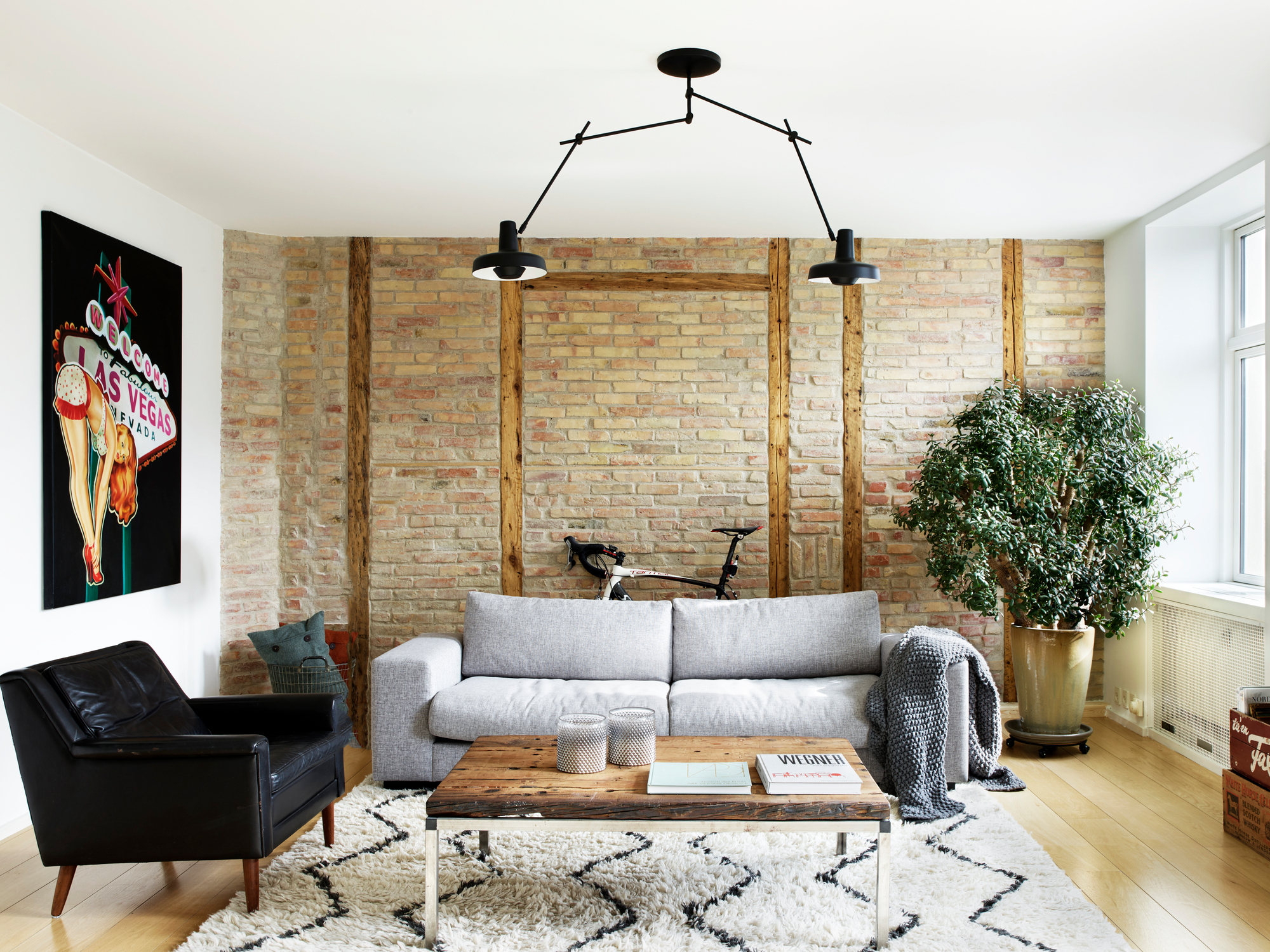 Wohnzimmer mit Arigato Deckenleuchte, schwarze Pendelleuchte über Sofa und Couchtisch.