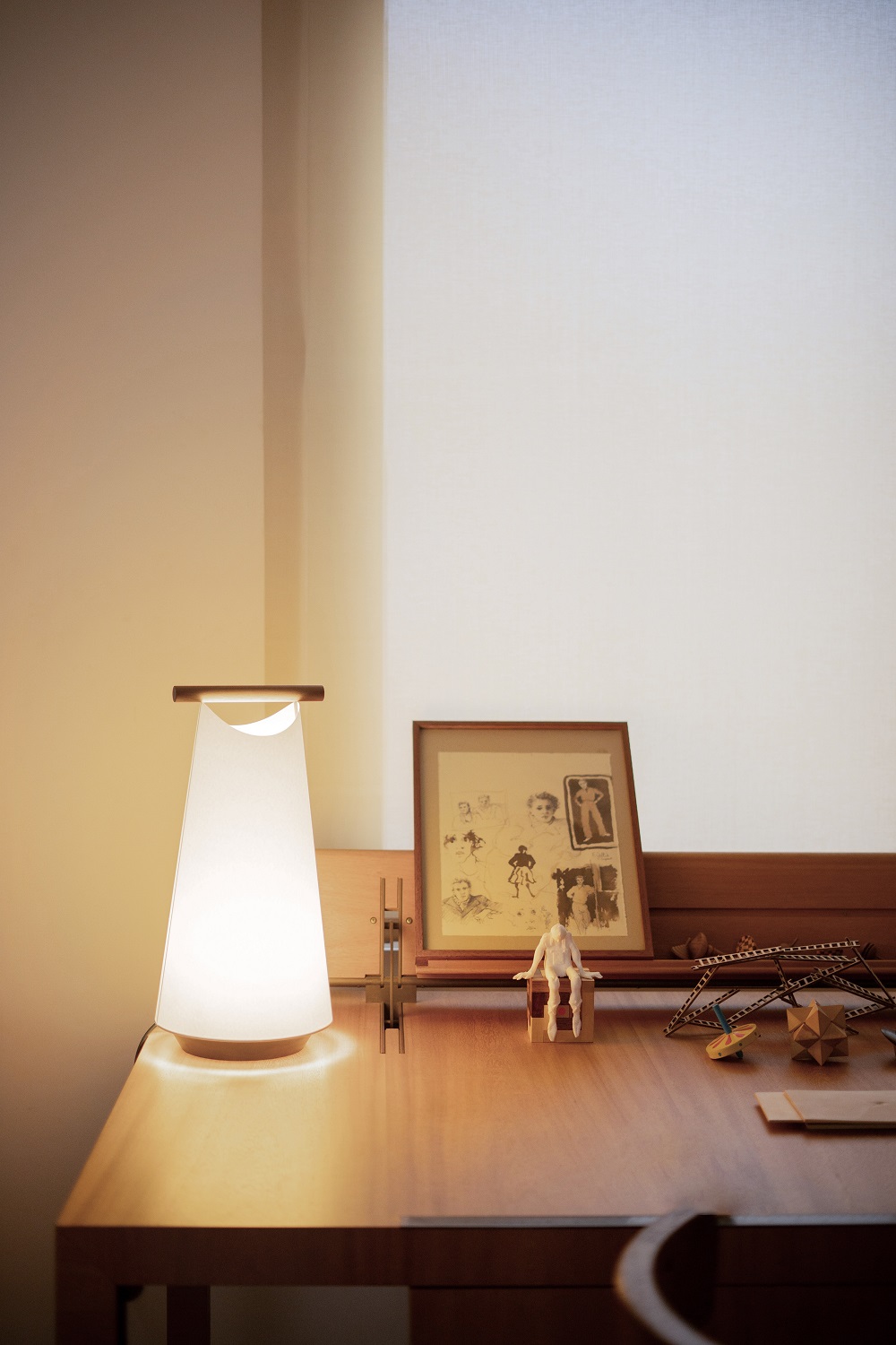 Catay Tischleuchte von Nomon auf einem Schreibtisch mit Dekoration, warmes Licht, minimalistisches Design.