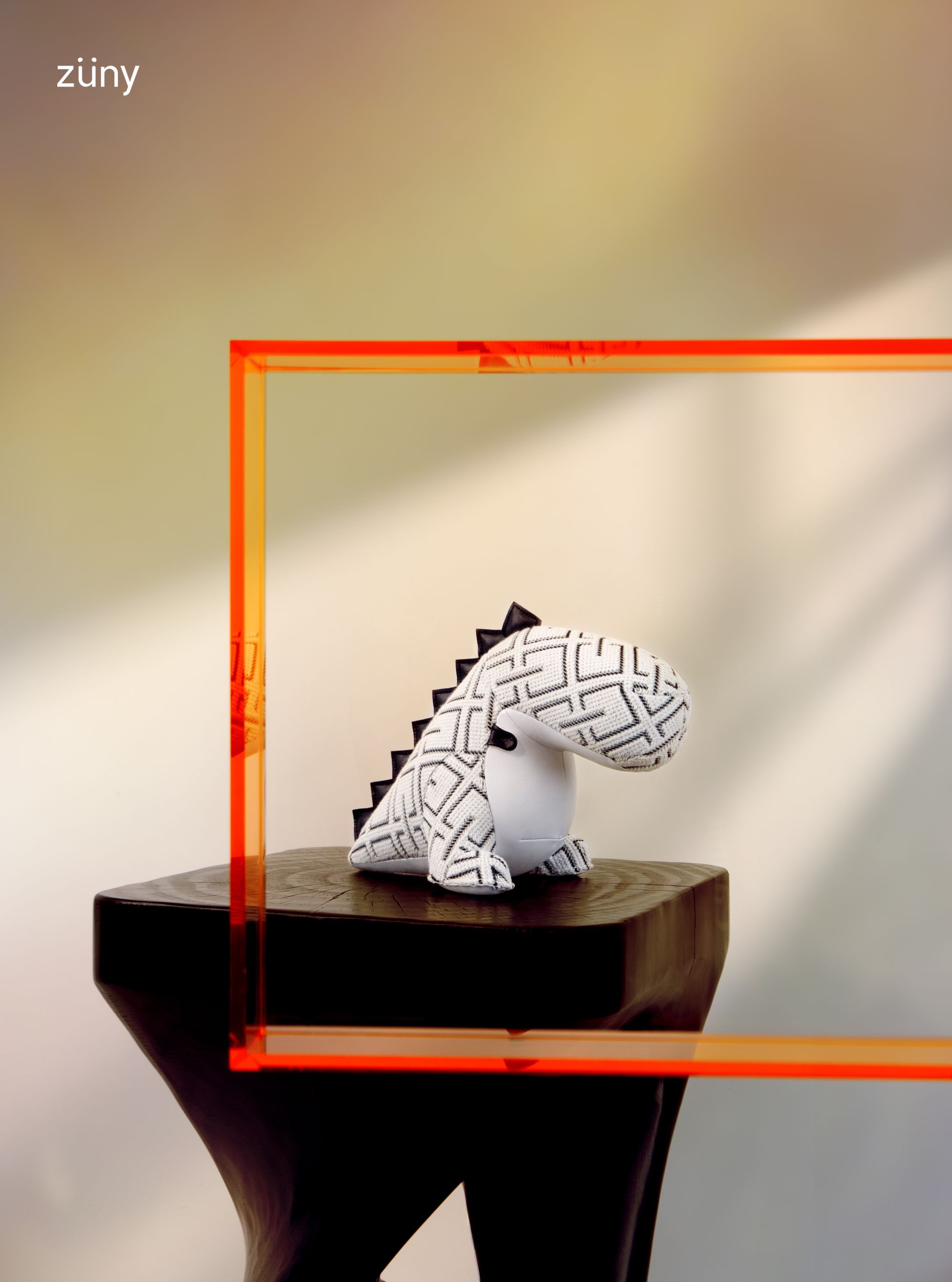 Weiße Züny x KVADRAT Dinosaurier Buchstütze Bobo Grid auf dunklem Holzsockel, umrahmt von orangefarbenem Rahmen.