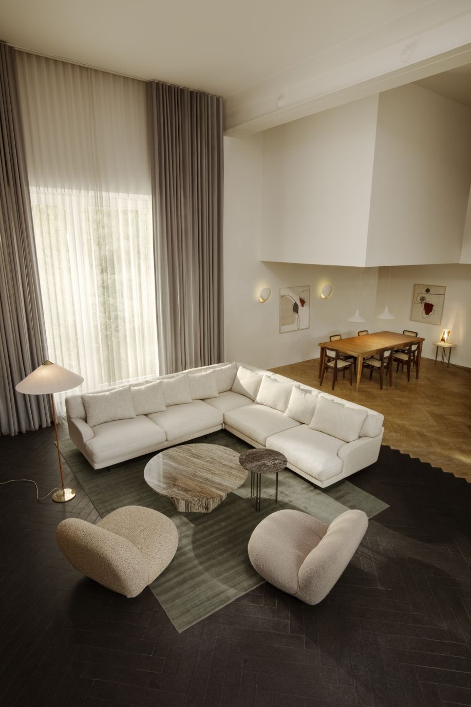 Helles Wohnzimmer mit Gubi Cobra Wandleuchten, großem Sofa, Teppich und Esstisch im Hintergrund.