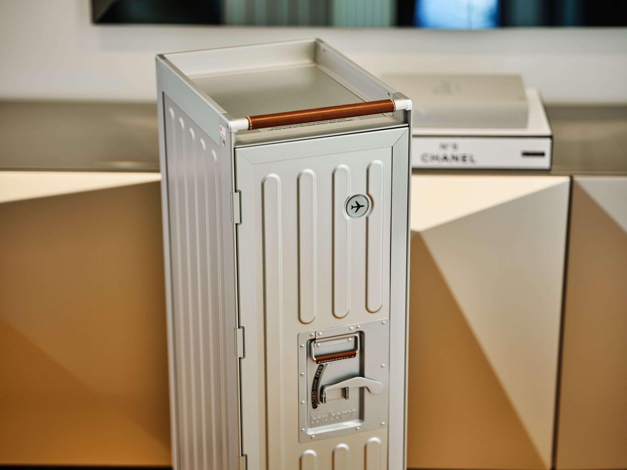Silberner Voyager Flugzeugtrolley Bordbar mit braunem Griff vor modernem Sideboard, ideal als Designmöbel und Hausbar.