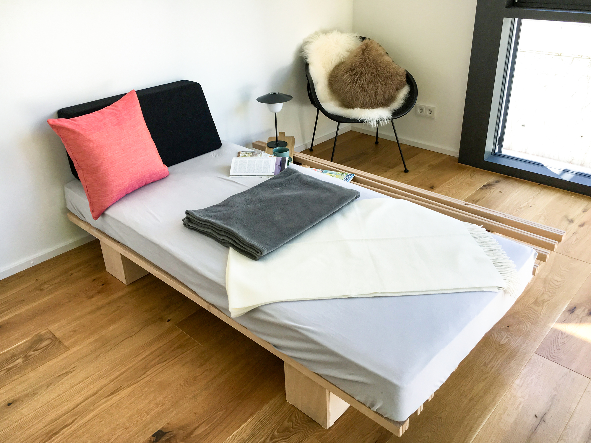 Tojo V Bett 90/180 aus Holz mit Matratze, Kissen und Decken in hellem Raum.