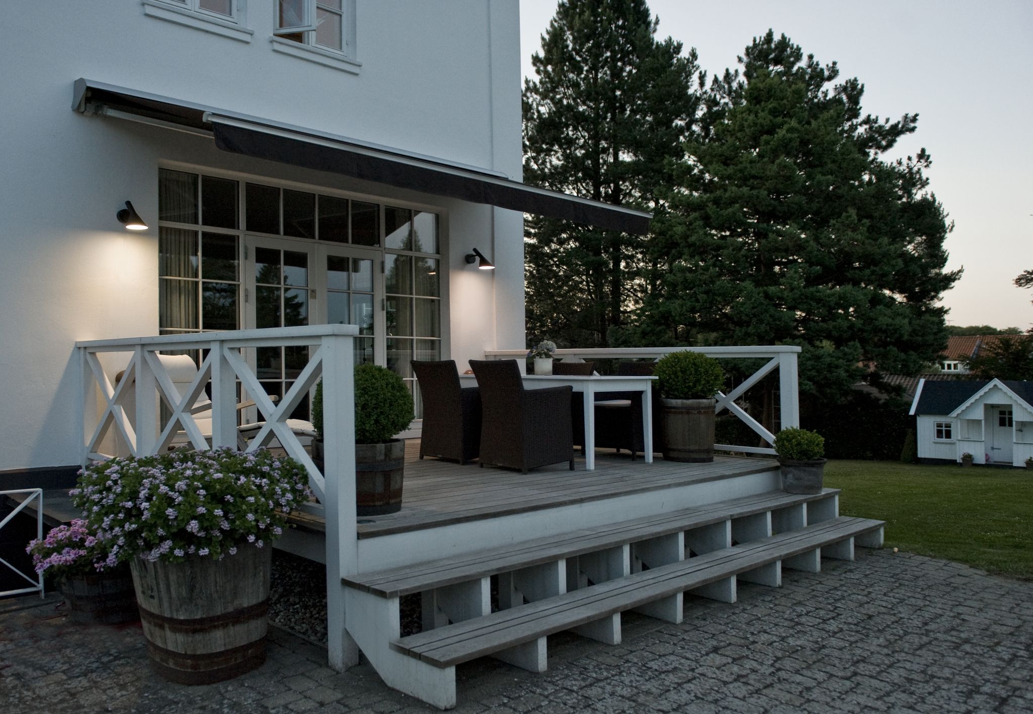 AJ 50 Wandleuchte von Louis Poulsen an weißer Hauswand überdachtem Terrassenbereich mit Tisch und Stühlen.