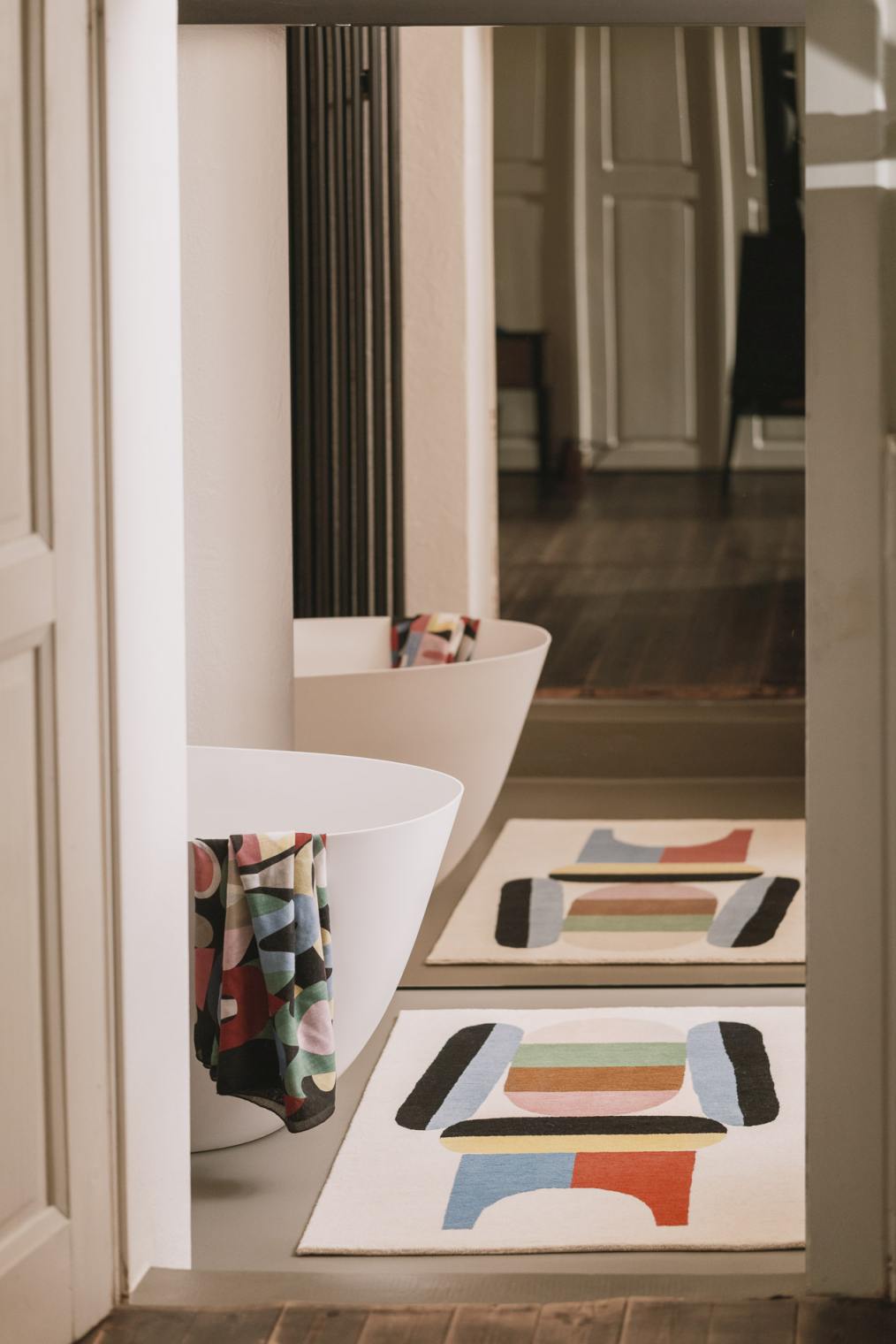 Zwei Elis Teppiche mit geometrischem Muster im Badezimmer, neben weißen Badewannen und bunten Handtüchern.