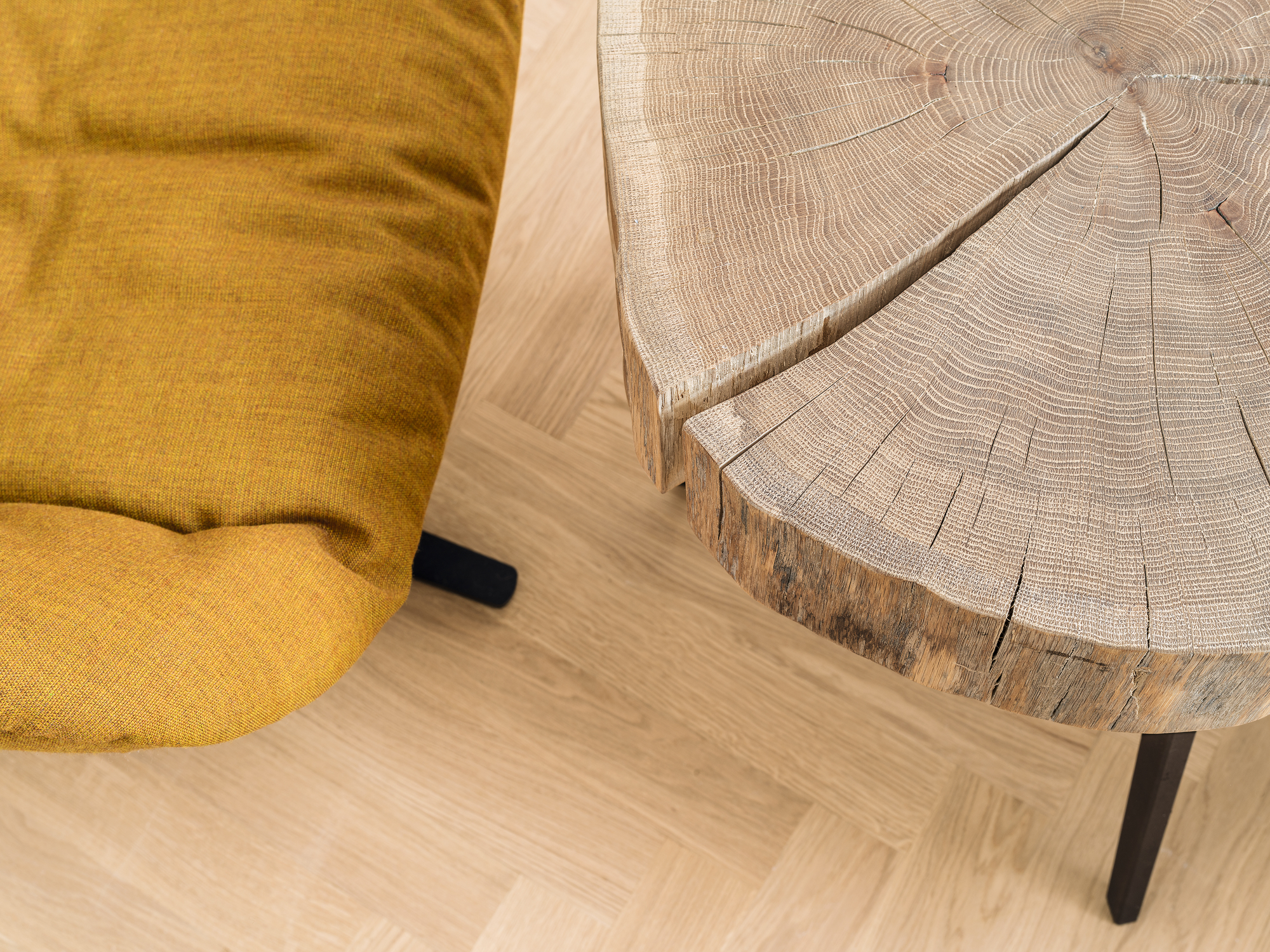 Nahaufnahme des Janua Stomp Beistelltisches H52 aus rohem Holz neben einem gelben Sessel.