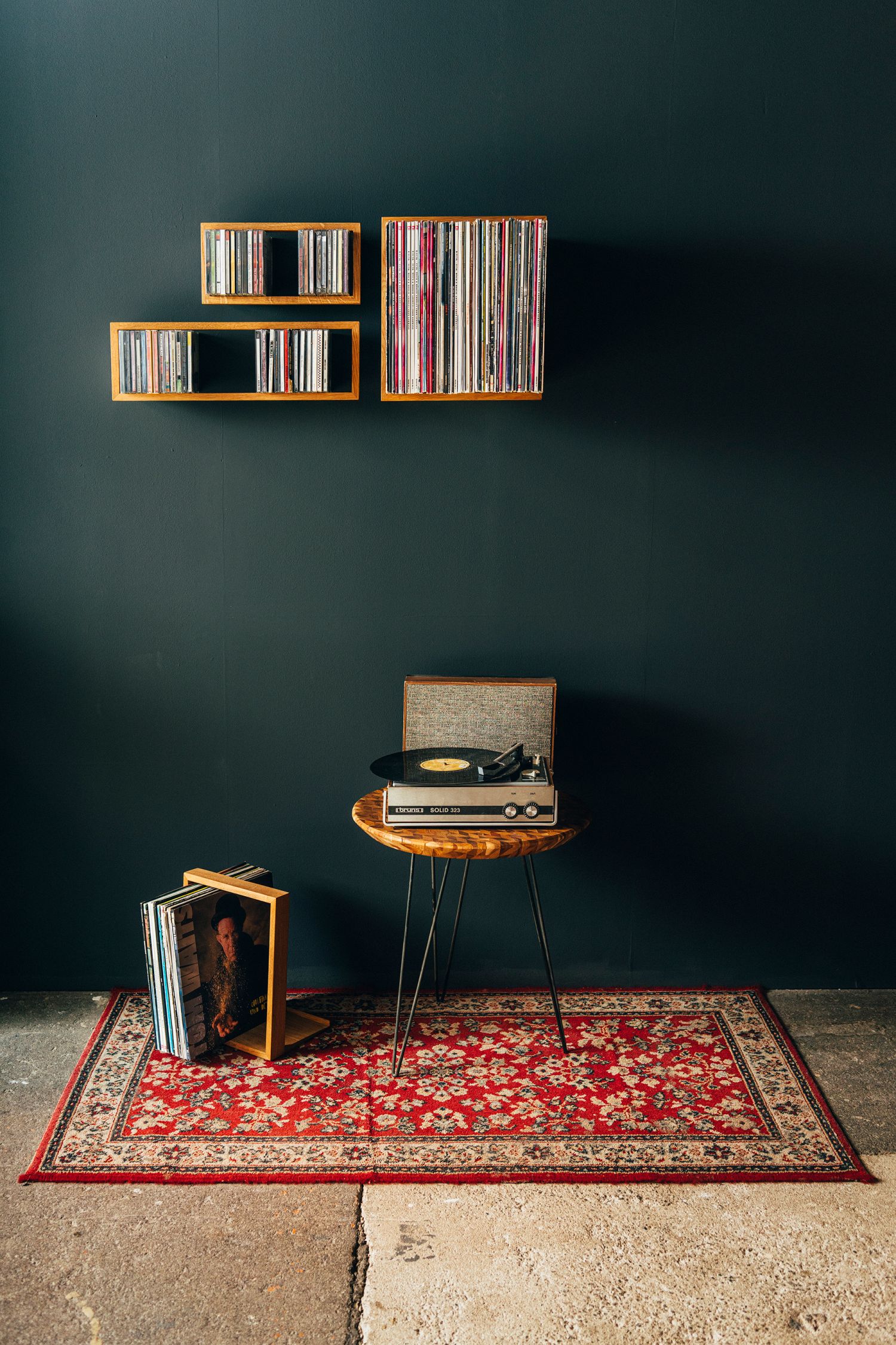 Wandmontiertes Vinyl b-platte Schalplattenregal "das kleine b" mit Schallplatten, Plattenspieler und Teppich auf dunklem Hintergrund.