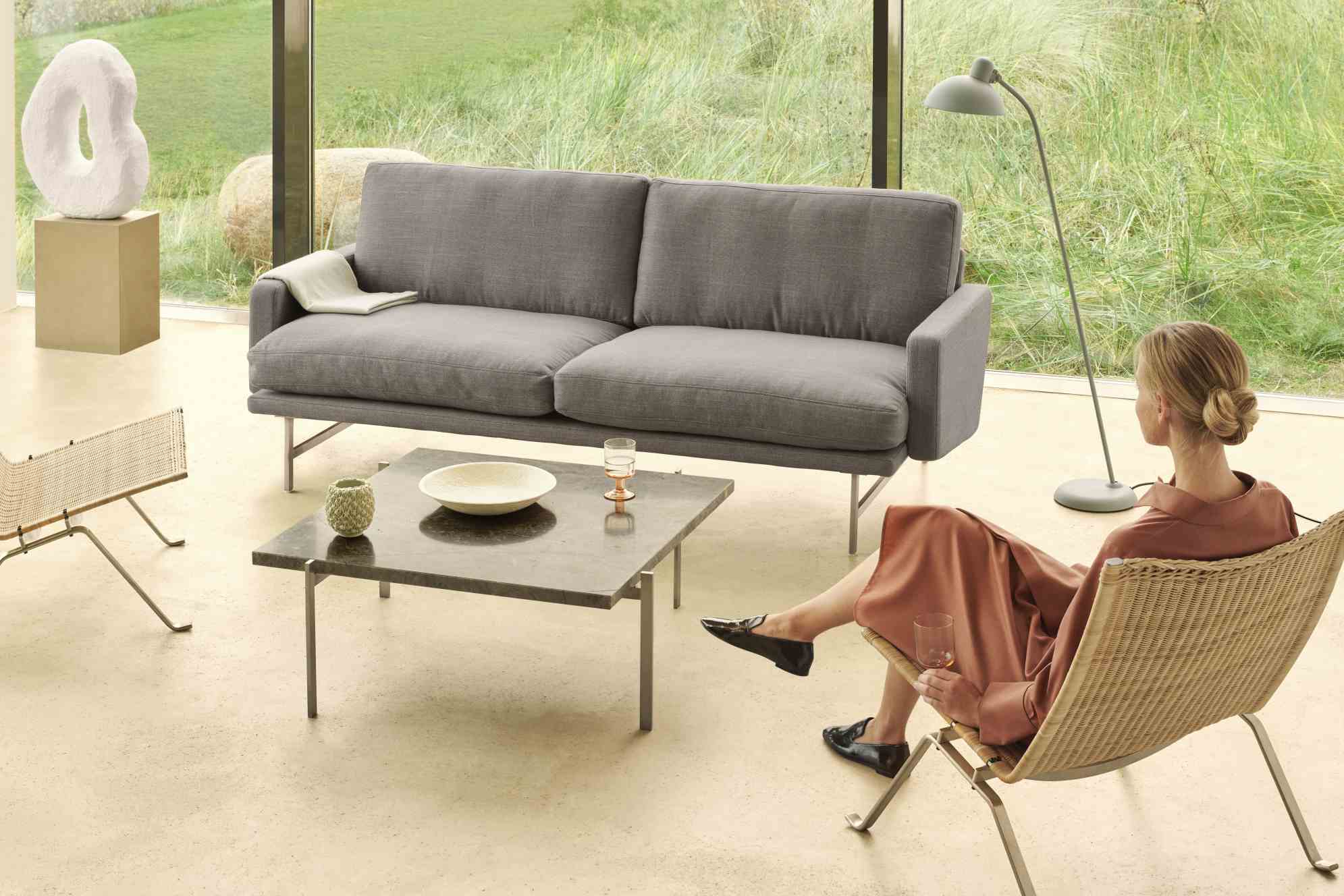 PK 61 Couchtisch von Fritz Hansen im modernen Wohnzimmer mit grauer Couch und Frau.