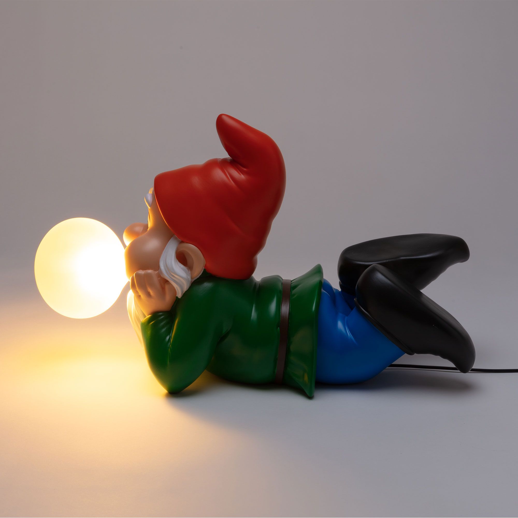 Gummy Dreaming Leuchte von Seletti: Liegender Gartenzwerg mit roter Mütze, der eine leuchtende Kugel hält.