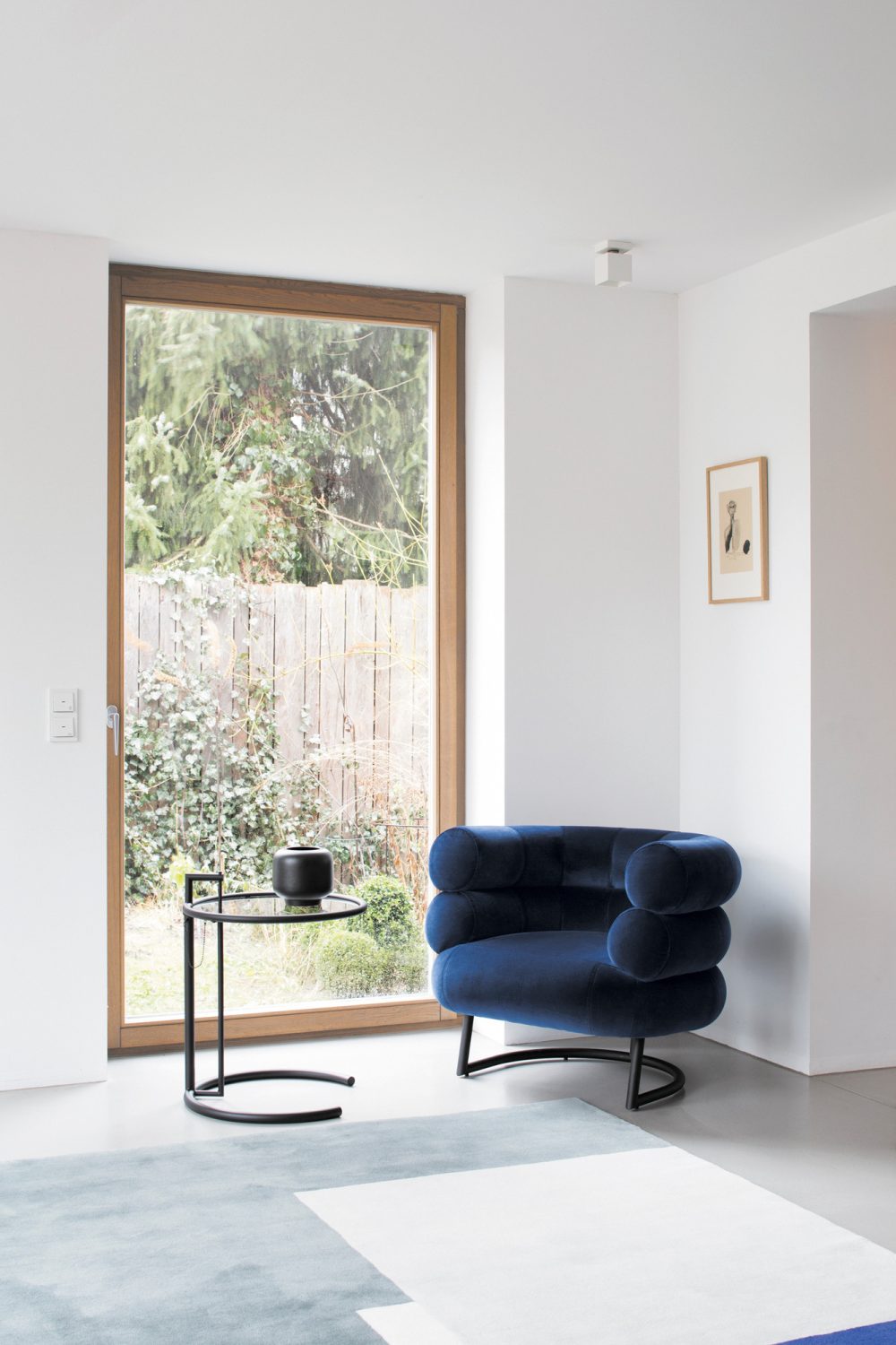 Blauer Samt Sessel mit rundem Design und schwarzem Beistelltisch in modernem Wohnzimmer.