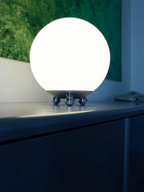 Moderne Tischleuchte mit runder, weißer Glaskugel und Chromfuß auf Kommode, stimmungsvolle Beleuchtung.