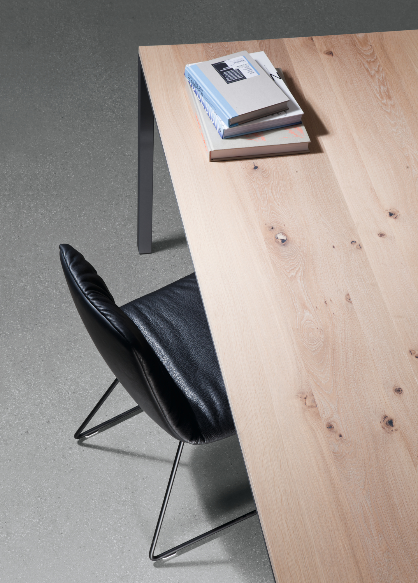 Detailaufnahme Janua S 600 Tisch Eiche mit Bücherstapel und schwarzem Lederstuhl, modernes Möbeldesign für Esszimmer und Büro.
