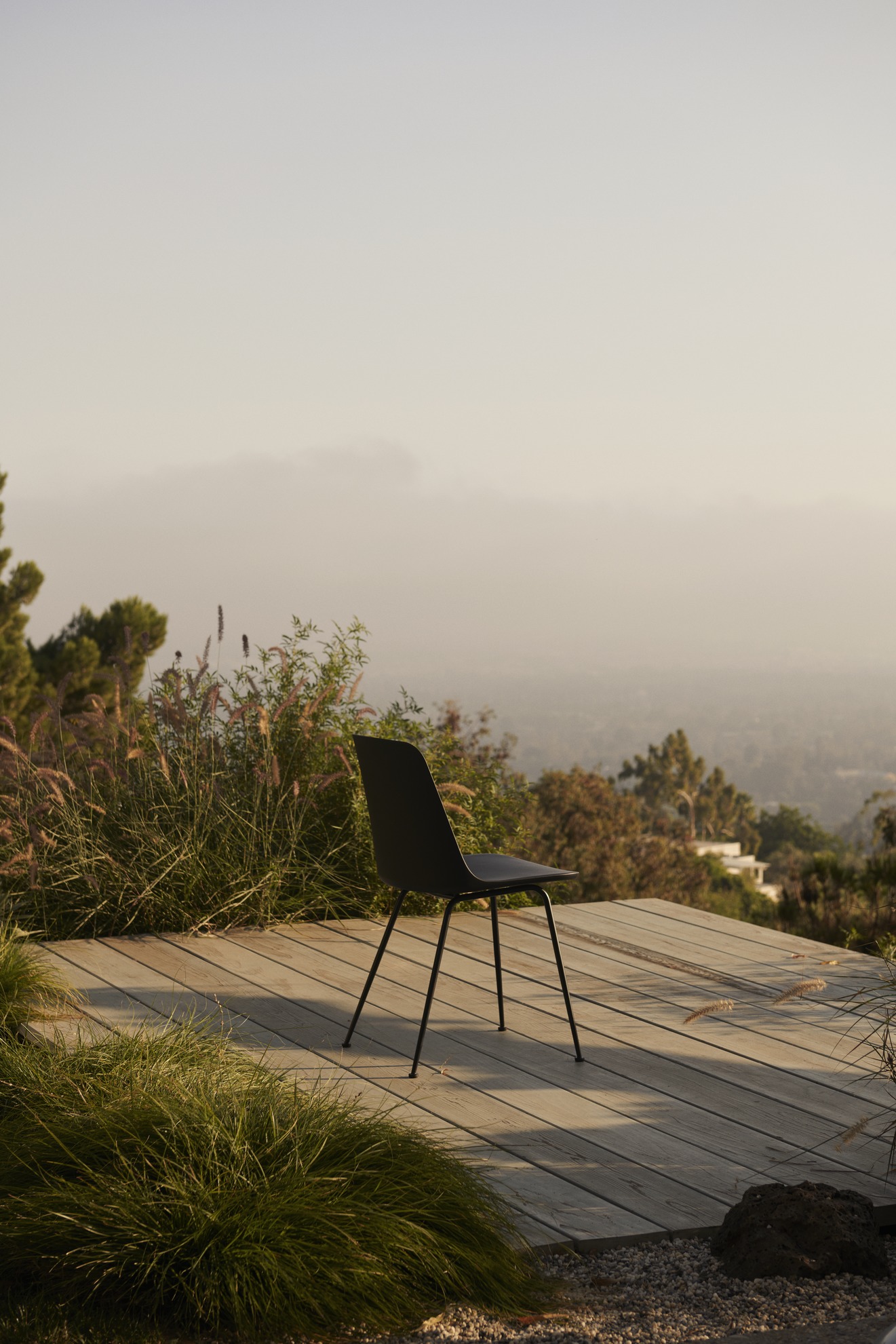 Schwarzer Rely HW70 Outdoor Stuhl von AndTradition auf Holzterrasse mit Blick auf die Landschaft.