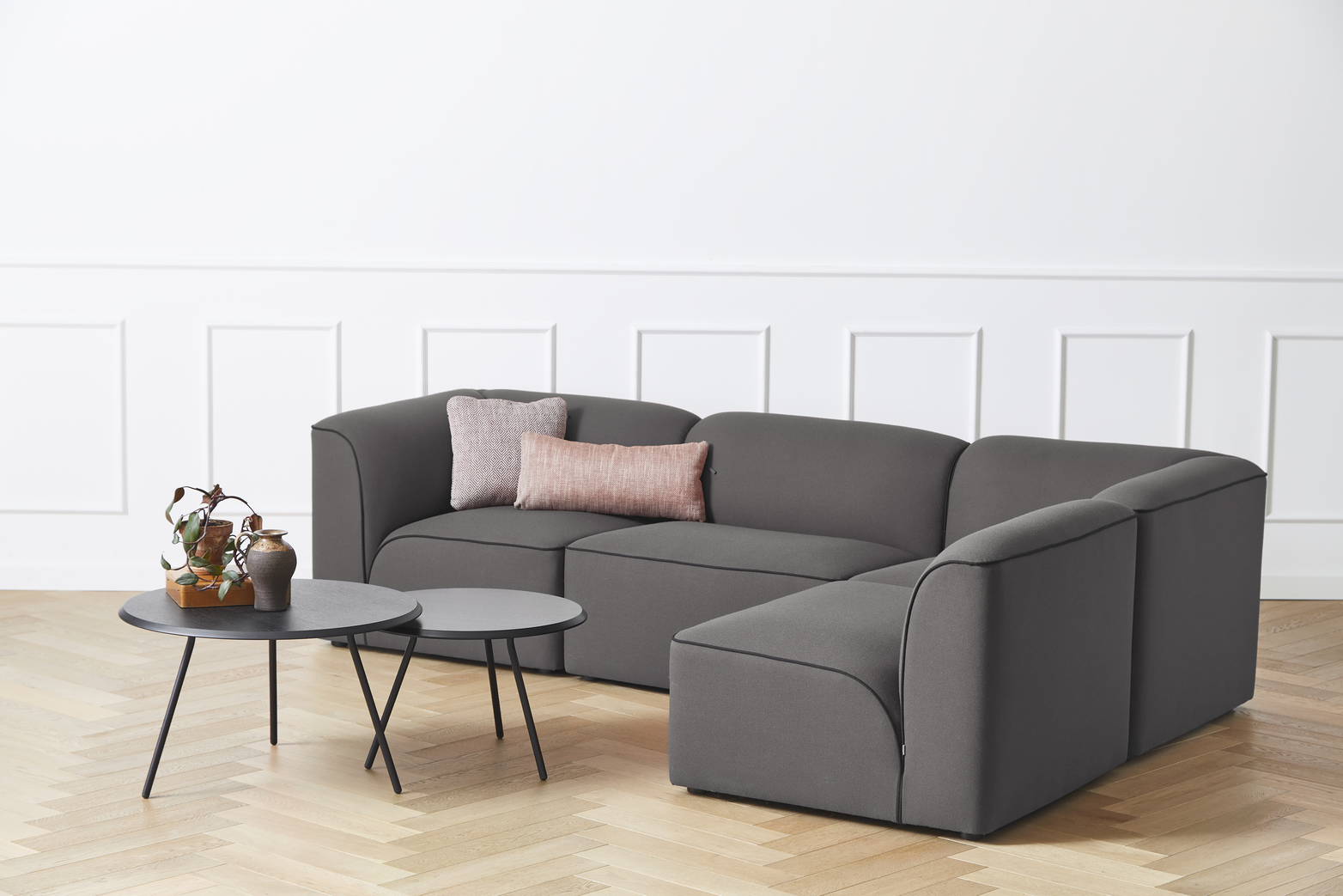Graues Flora Modulsofa von Woud mit Kissen und Beistelltischen auf hellem Holzboden.
