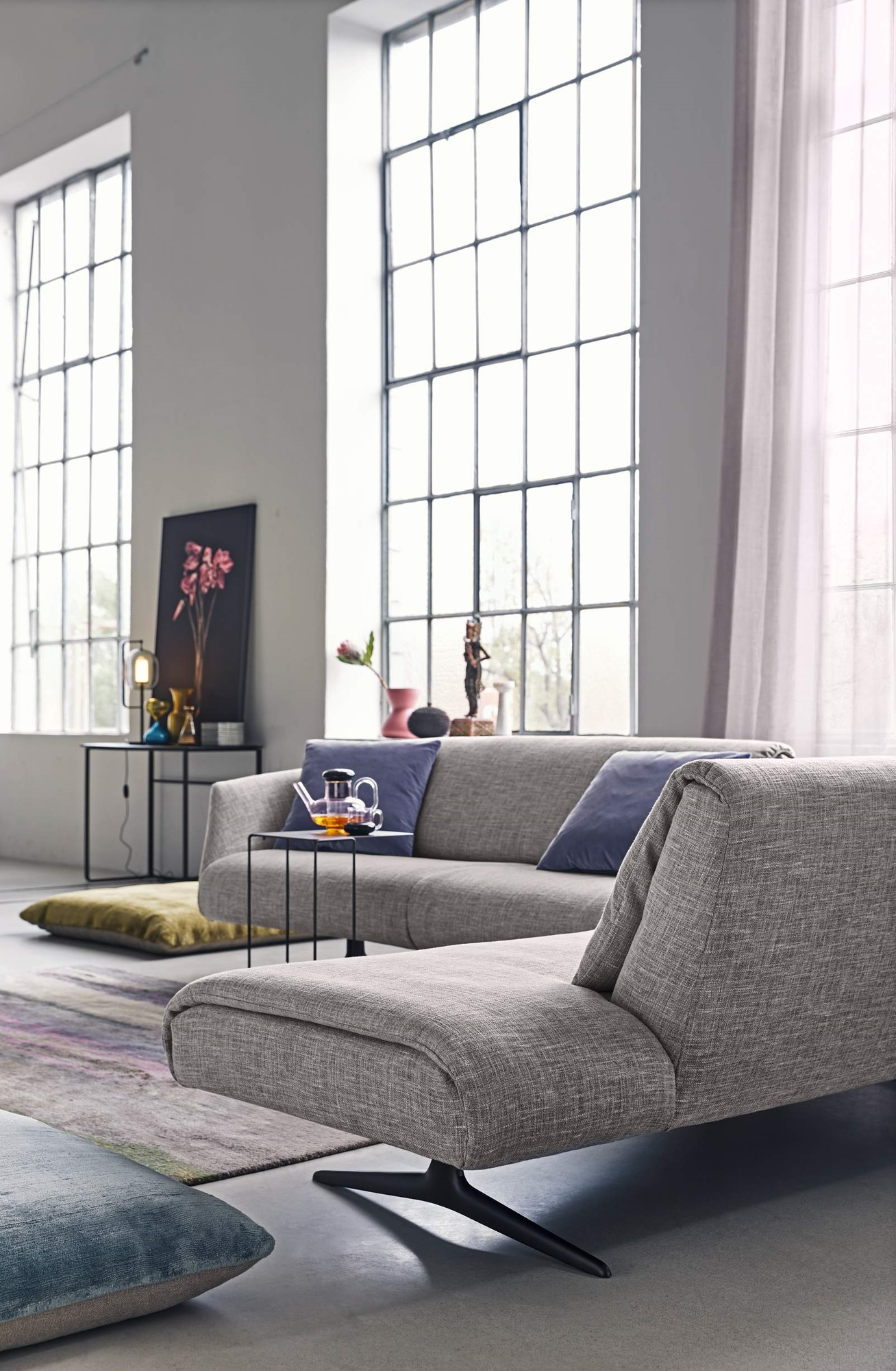 Oki Beistelltisch von Walter Knoll neben grauer Couch in modernem Wohnzimmer mit großen Fenstern.