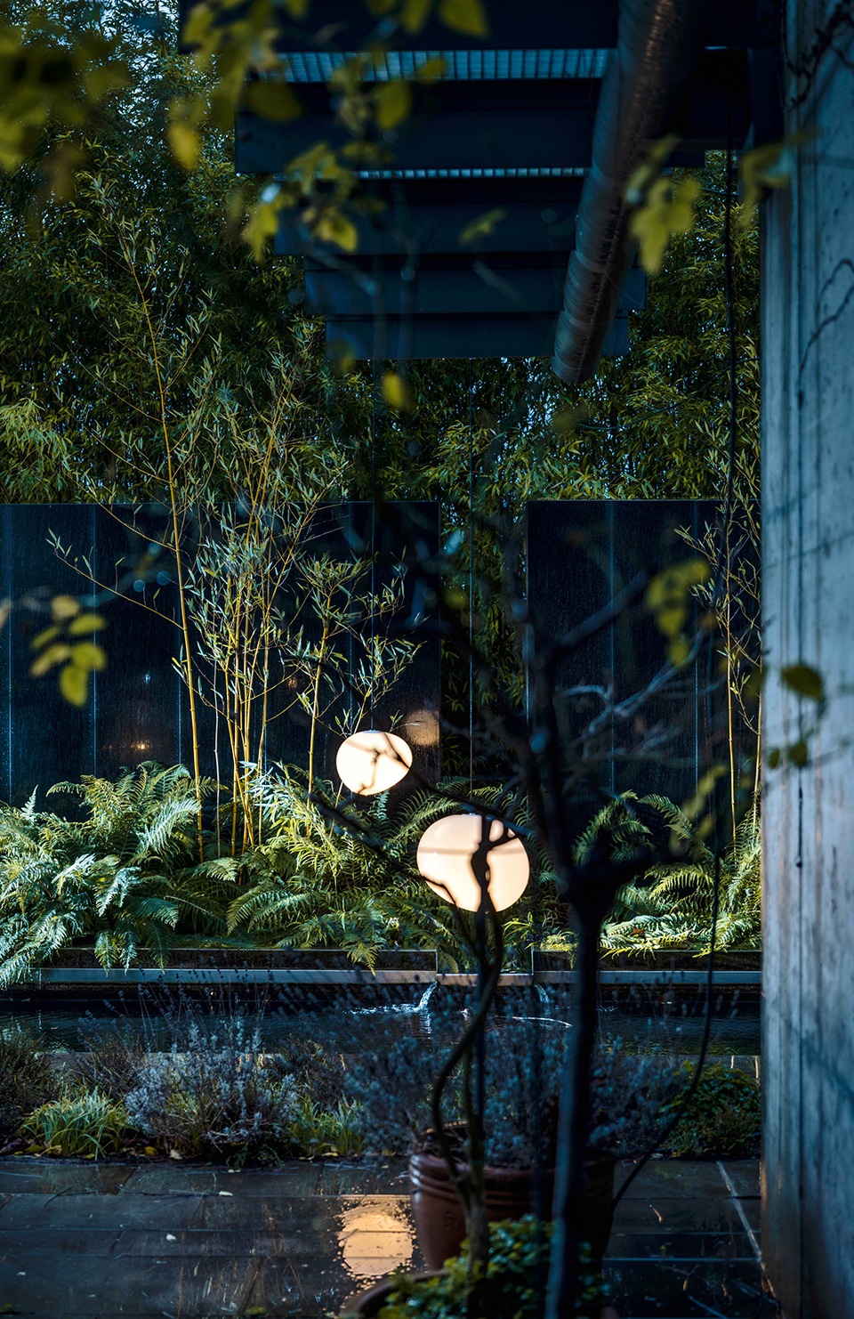 Zwei Gregg Pendelleuchten von Foscarini beleuchten einen üppigen Garten mit Teich und Bambus.