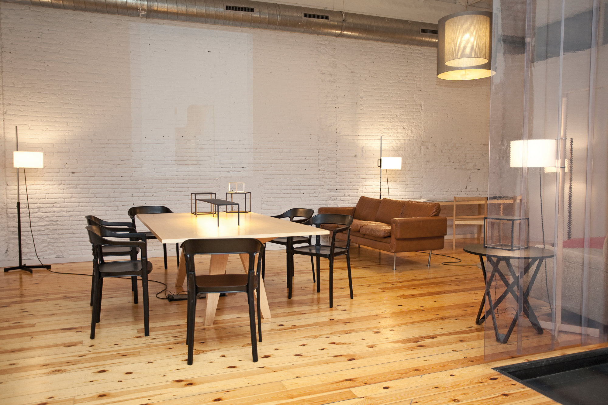 Helle, moderne Wohnraum-Szene mit Santa & Cole TMC Stehleuchten, Esstisch mit Stühlen und braunem Ledersofa.
