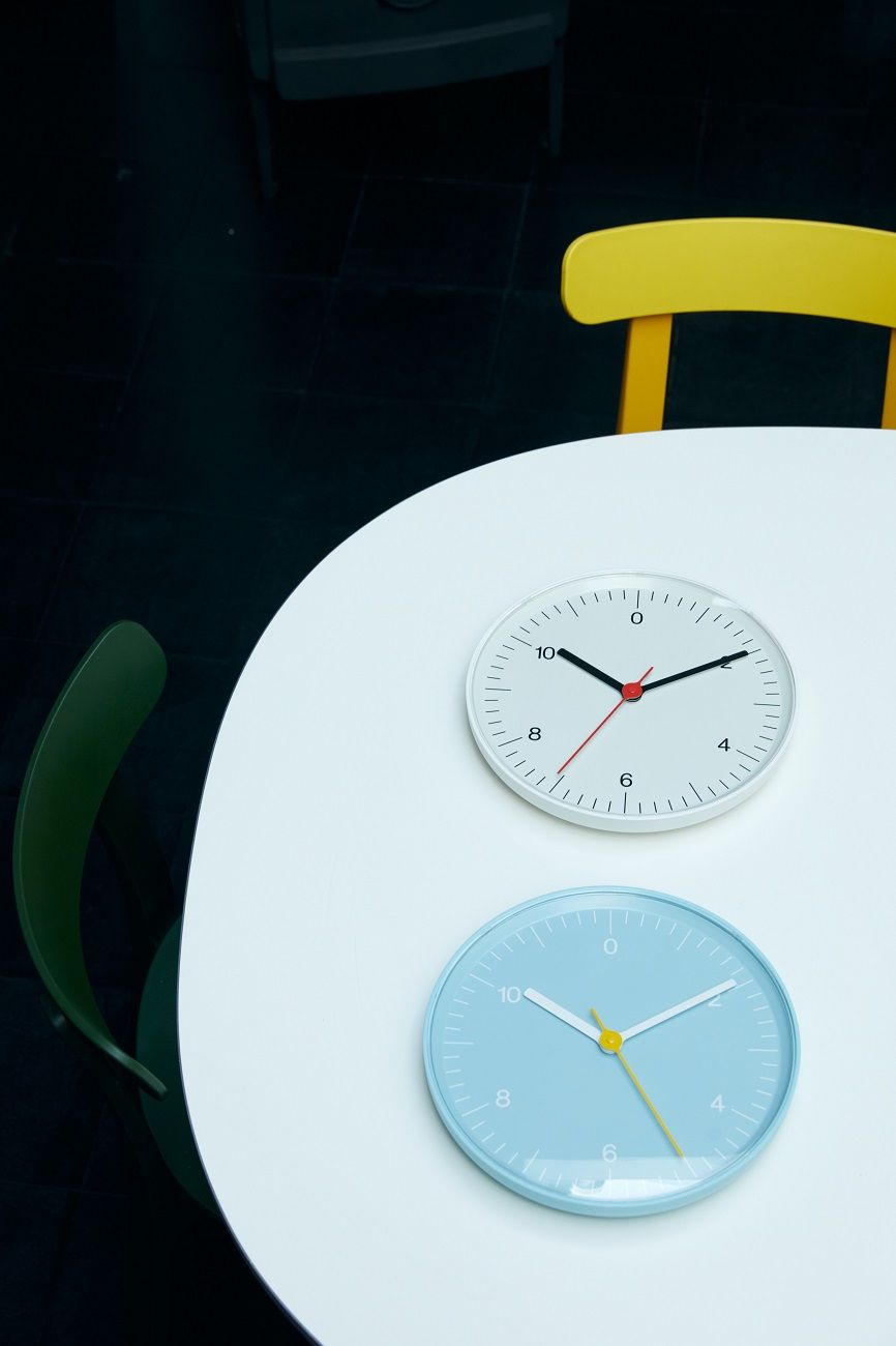 Zwei moderne Hay Wanduhren auf einem weißen Tisch, eine schwarz-weiße und eine hellblaue Uhr.