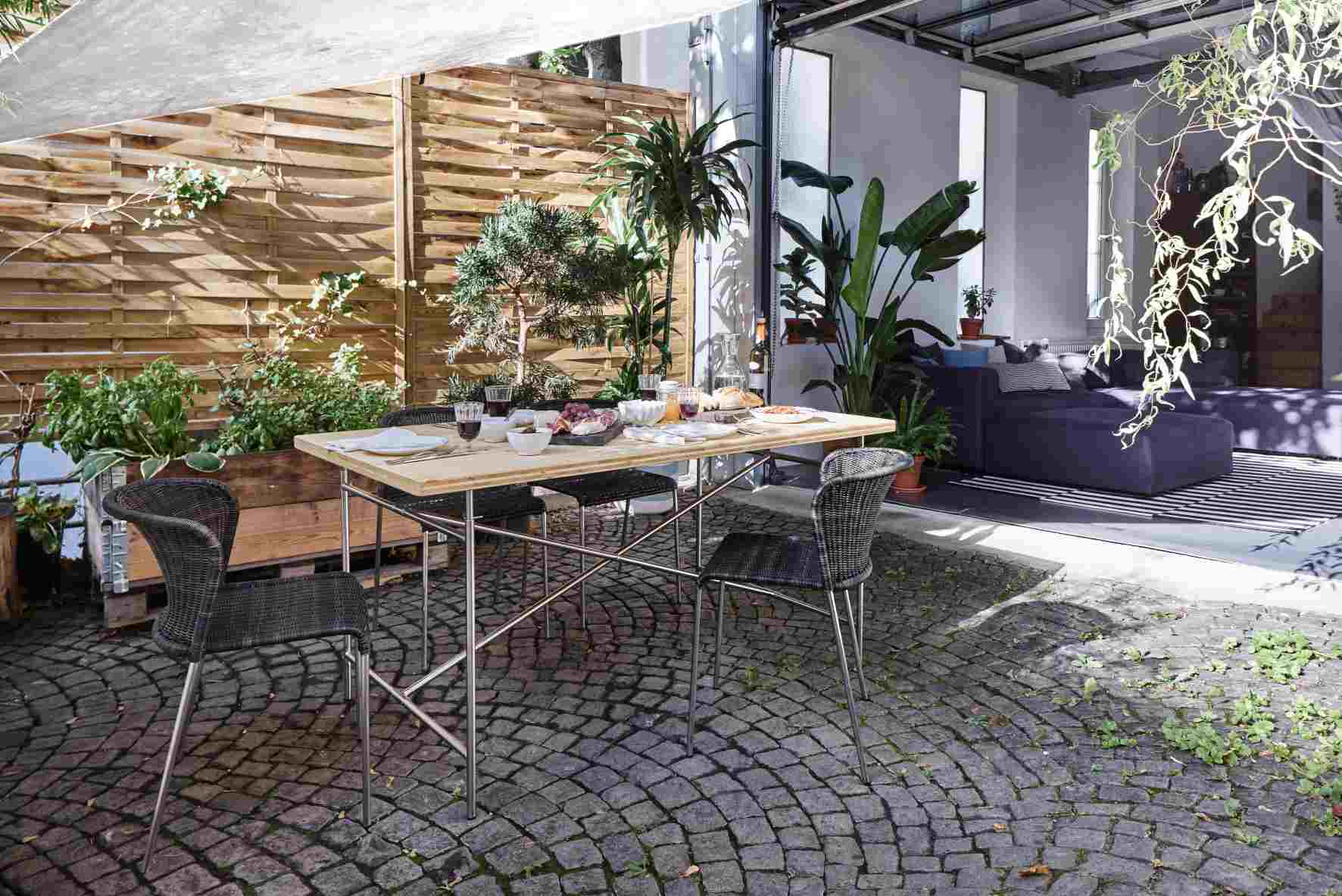 Eiermann Tisch mit heller Tischplatte und schwarzen Stühlen im Garten, gedeckt mit Speisen.