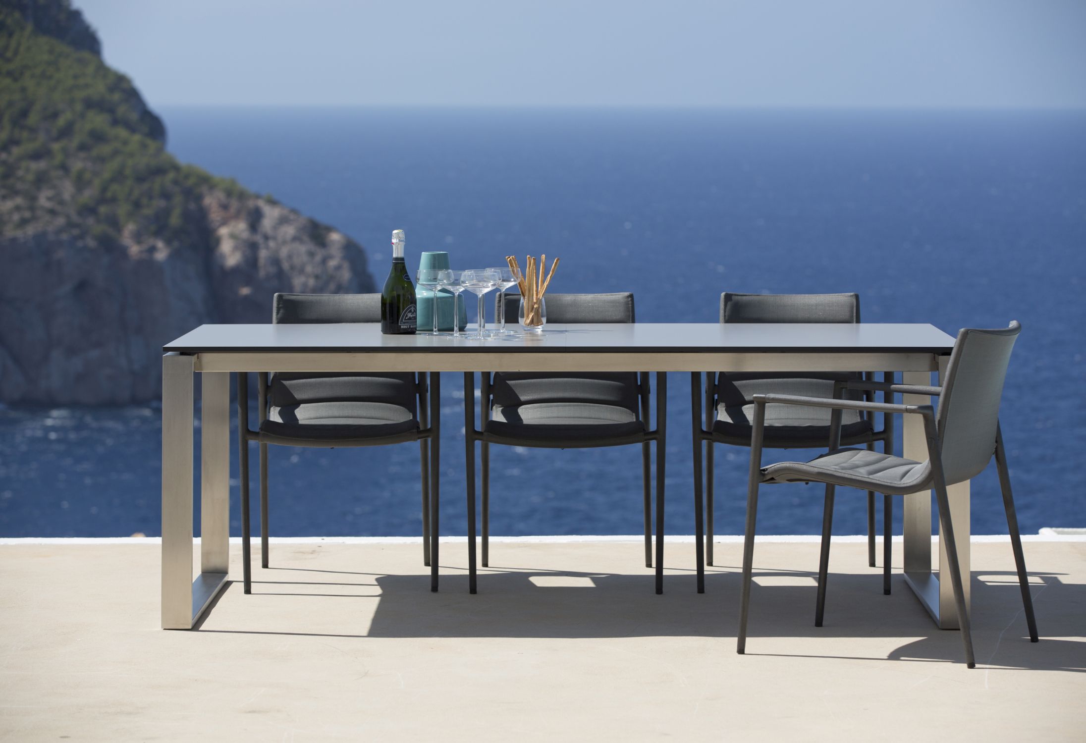 Core Outdoor Stuhl AirTouch von Cane-Line in Taupe mit Armlehnen am Esstisch im Freien.