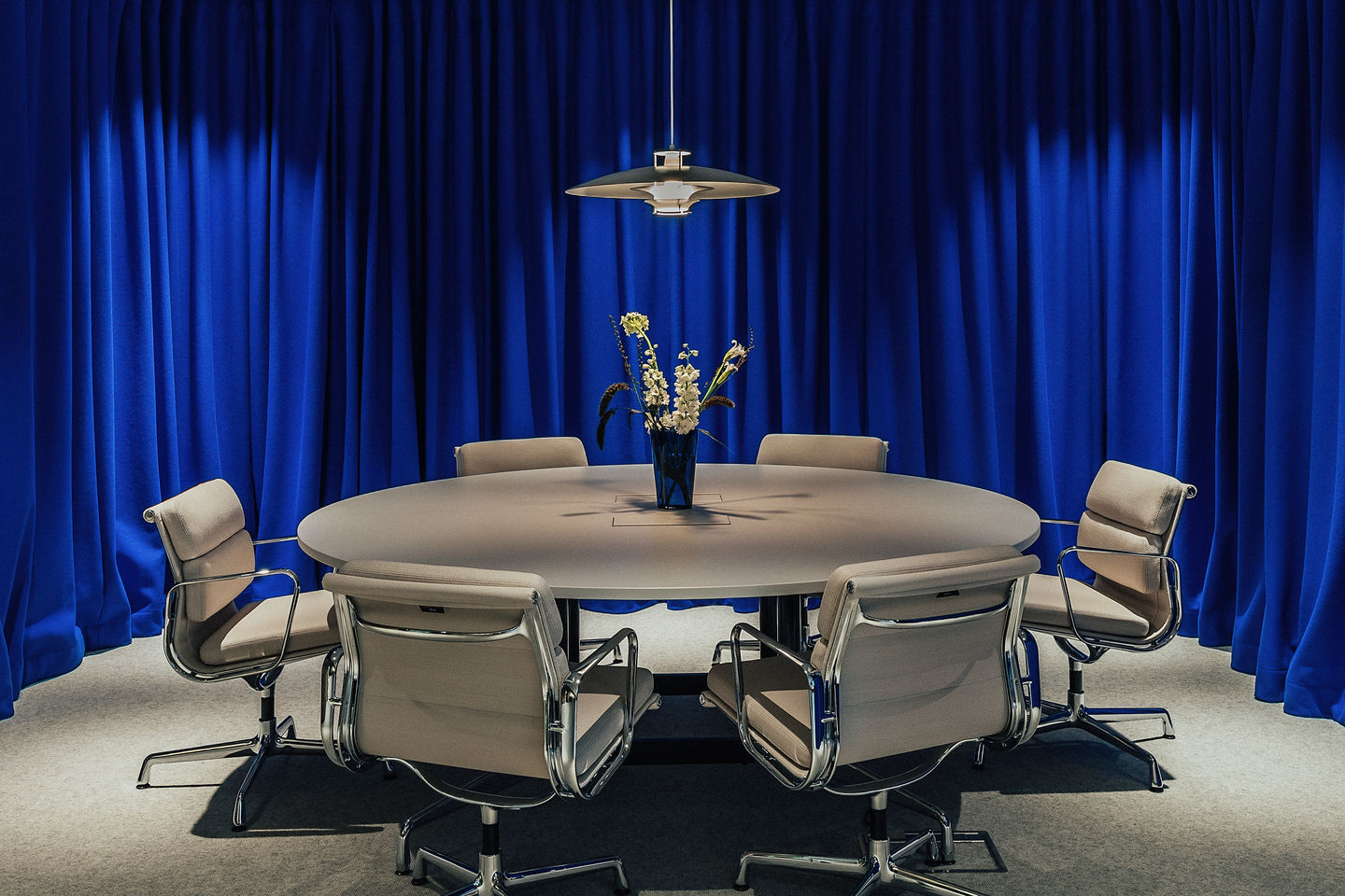 Konferenzraum mit rundem Tisch und sechs Vitra EA 207 Soft Pad Sesseln vor blauem Vorhang.