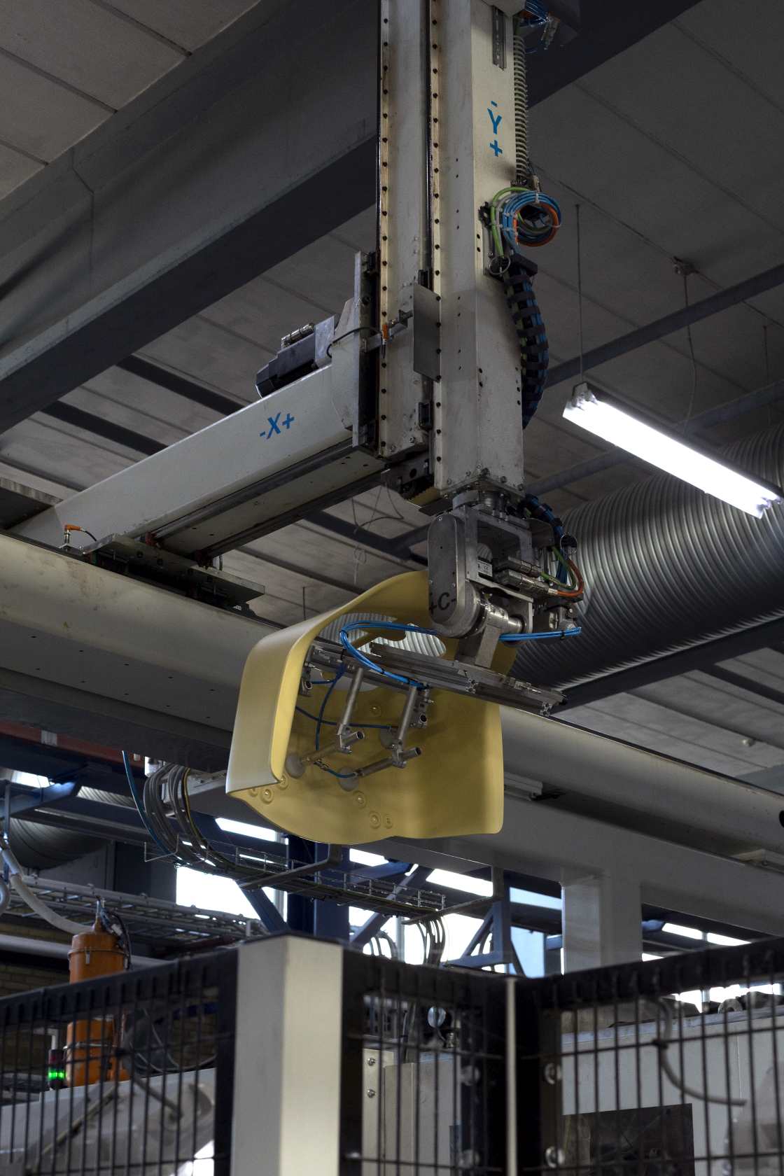 Industrieroboterarm mit gelbem Werkstück in einer Fabrikhalle, automatische Fertigung und Produktion.