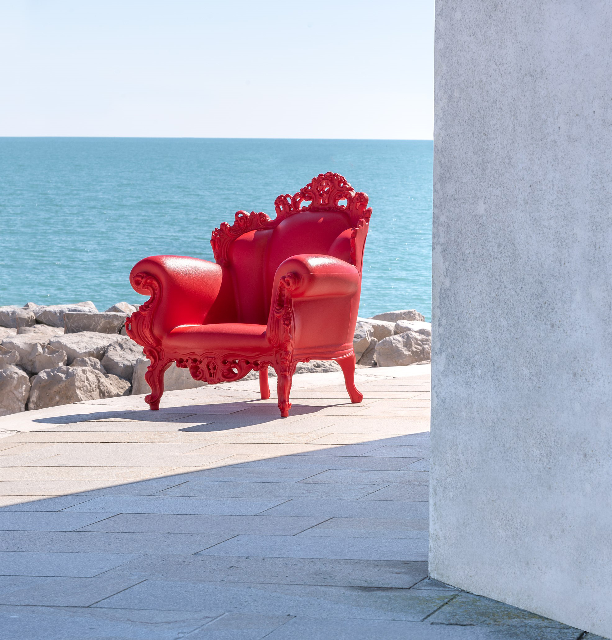 Roter Magis Proust Sessel für den Außenbereich vor blauem Meer und Felsen.