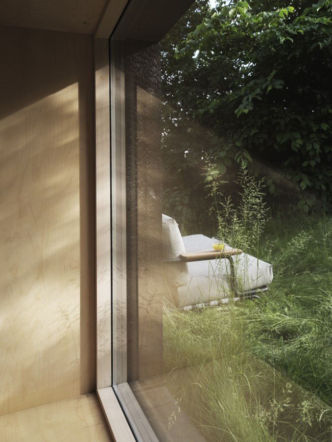 Settle Outdoor Sofa von Muuto, ein bequemes 2-Sitzer Gartensofa im Grünen, gesehen durch ein Fenster.