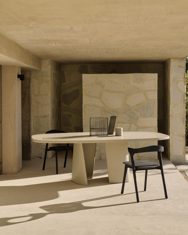 Canyon Outdoor Esstisch von Ethnicraft, oval, aus Beton mit zwei schwarzen Stühlen auf Terrasse.