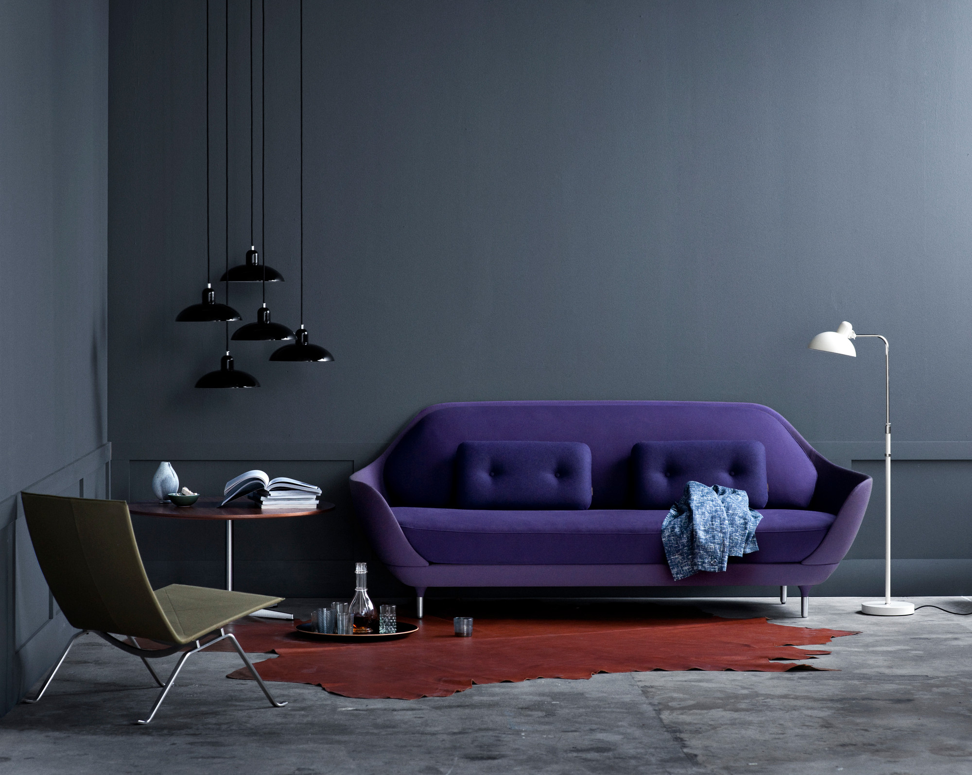 Wohnzimmer mit schwarzer Kaiser idell Pendelleuchte und lila Sofa von Fritz Hansen.