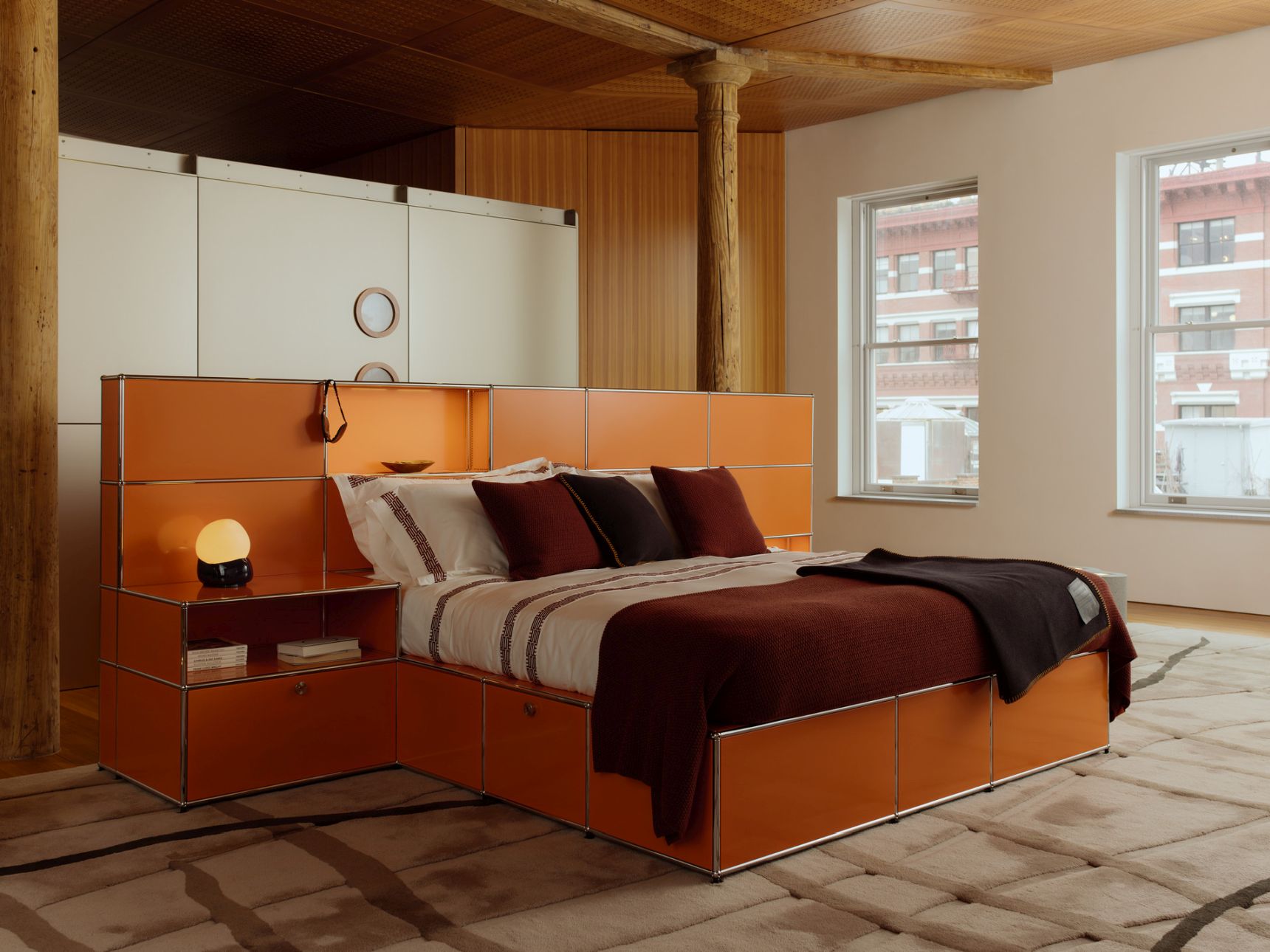 Orangefarbenes USM Haller Bett mit Schubladen und Nachttisch im Schlafzimmer.