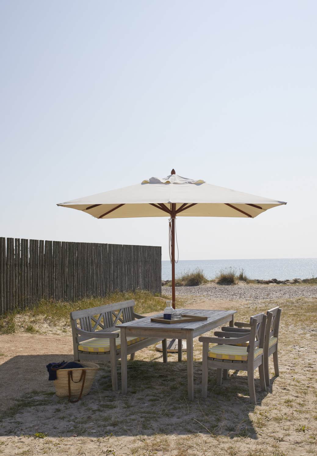 Drachmann Esstisch Outdoor von Skagerak by Fritz Hansen mit Bank und Stühlen am Strand.