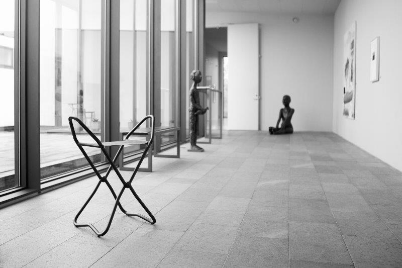 Schwarzer Faltstuhl aus Metall im Museum, minimalistisches Design, moderne Sitzgelegenheit für Kunstausstellungen und Galerien.
