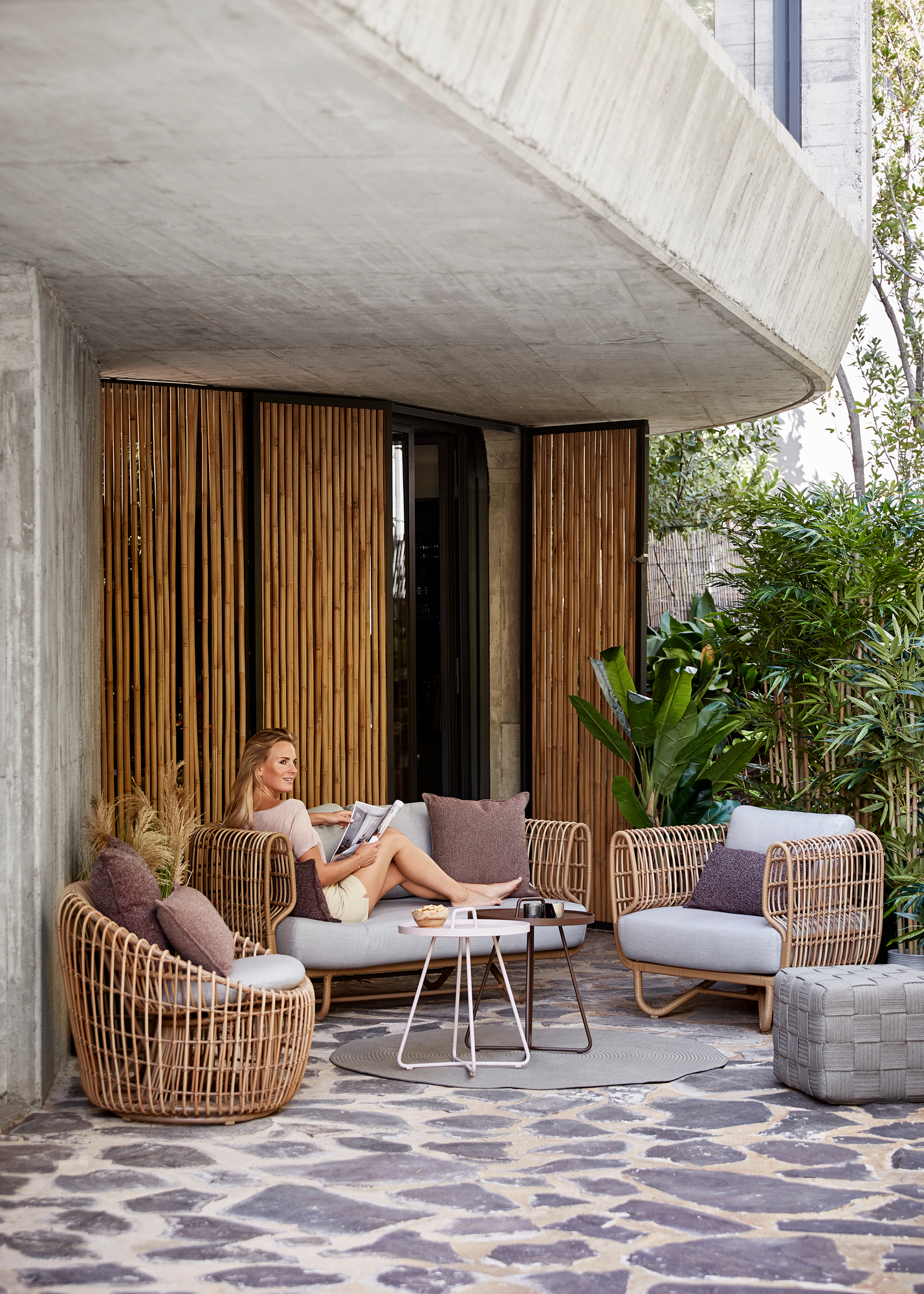 Frau entspannt auf Cane-Line Nest Outdoor Sofa mit Rattan-Sessel und Beistelltisch.